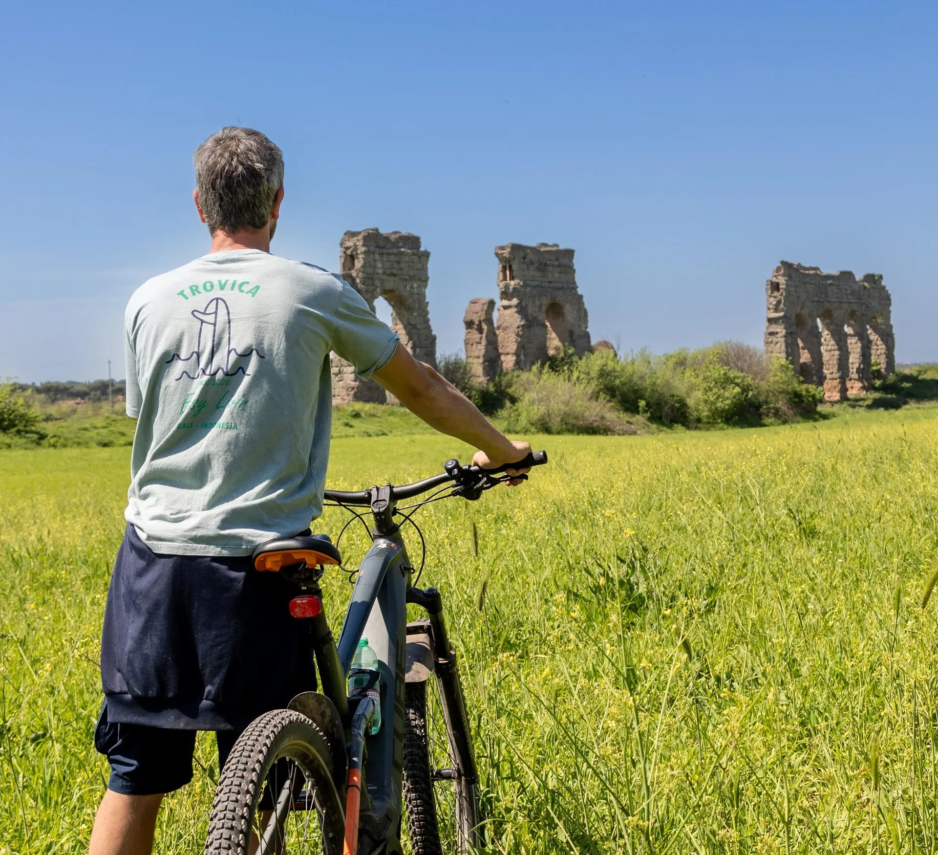 A cyclist stopped in a meadow looking at the ruined aqueduct