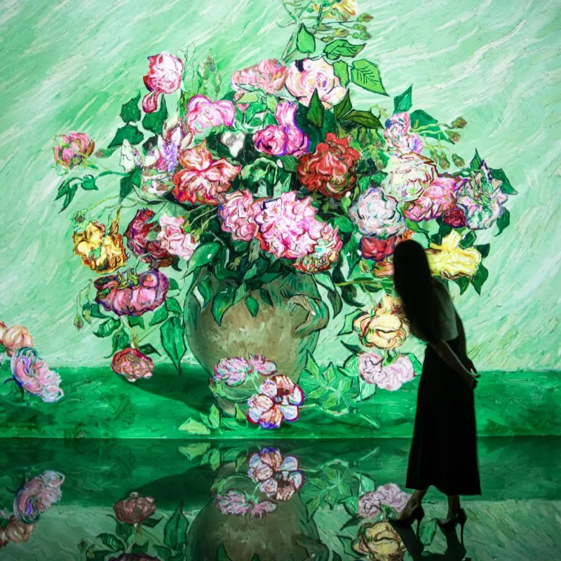 ゴッホ風に描かれたバラの花束が投影され、光沢のある床に花が映り込む前に、来館者が立っている
