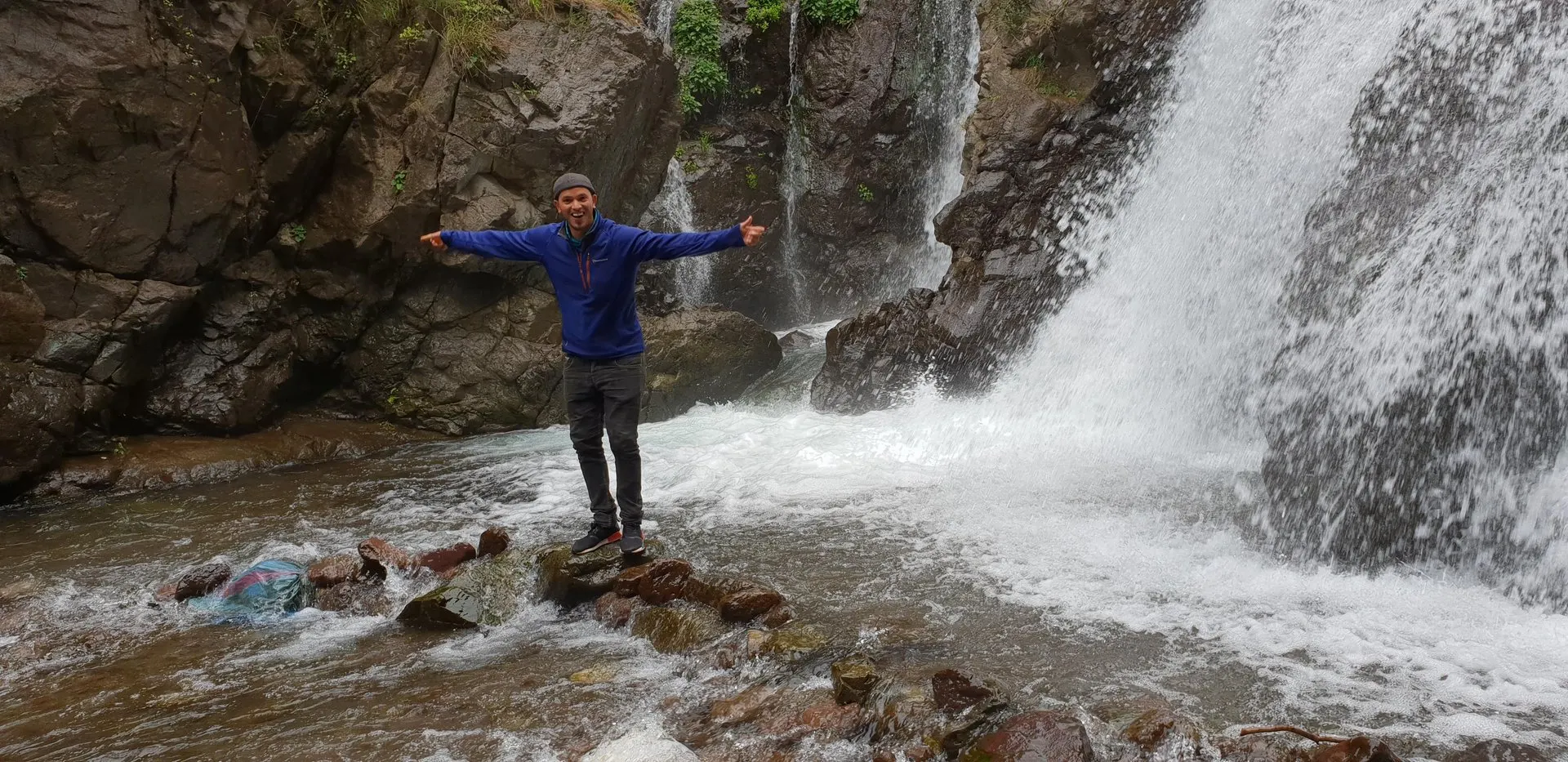 A visitor standing on stones in a mountain stream at the foot of a waterfall