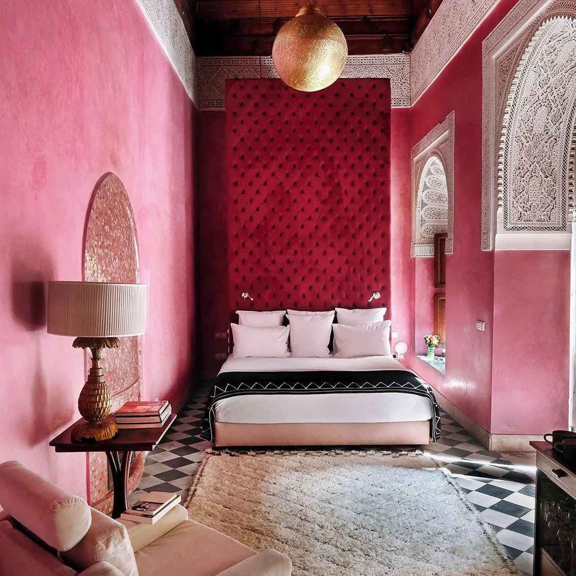 Large Room at El Fenn: a double bed under a tall red tufted headboard in a pink room with carved plaster arches and a cream rug