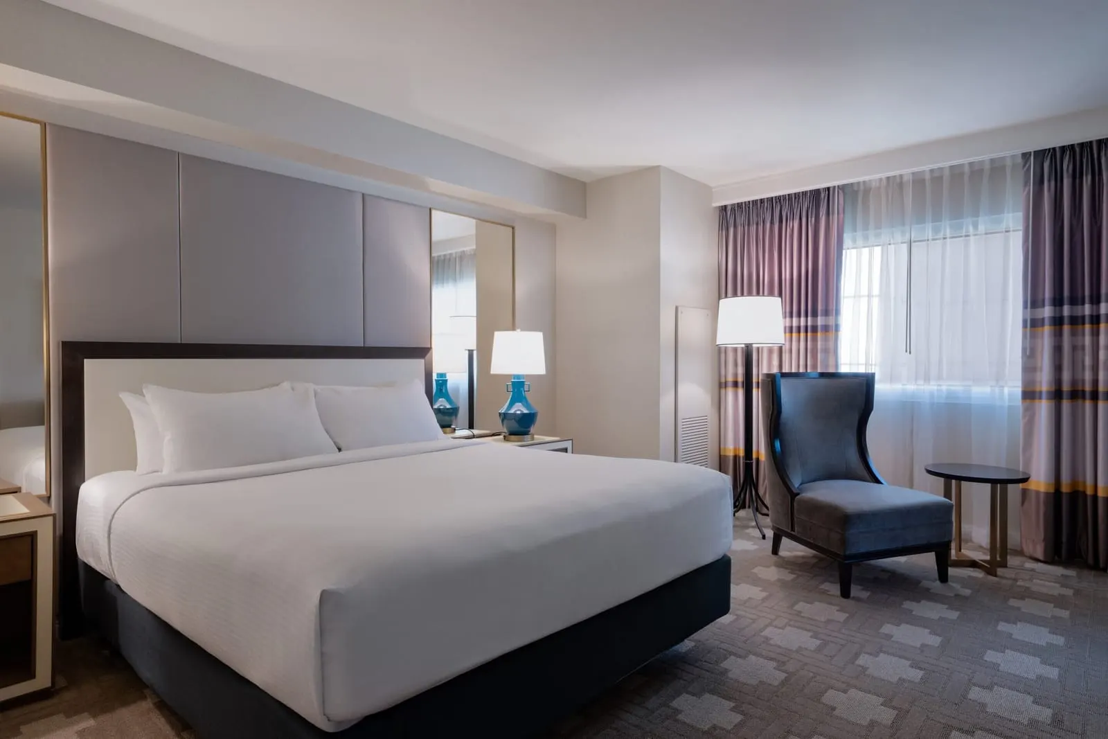 Julius Premium Studio Suite im Caesars Palace: ein Kingsize-Bett mit blauen Lampen, ein dunkler Sessel und ein kleiner Tisch am Fenster