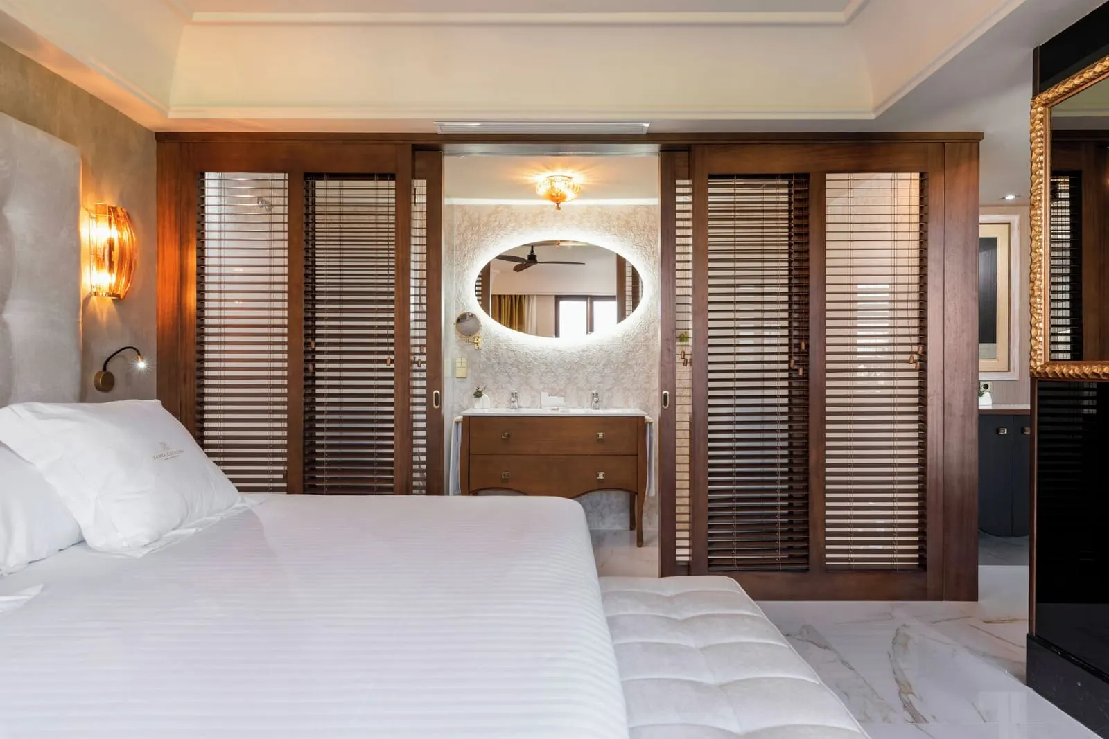 Junior Suite at Santa Catalina, a Royal Hideaway Hotel: the bed facing slatted wooden sliding doors that open on to a washbasin under an oval lit mirror