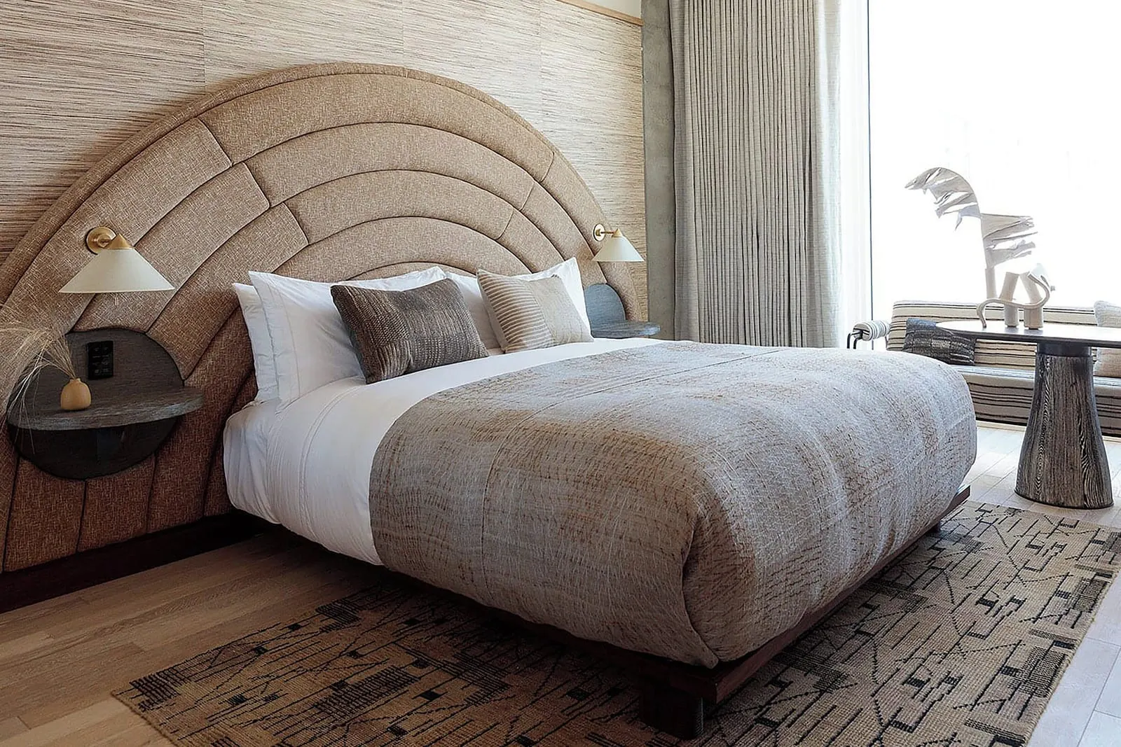 Premier Balcony King im Santa Monica Proper Hotel: ein Kingsize-Bett mit einem bogenförmigen Kopfteil und Nachttischregalen, mit einem Fenster mit Vorhängen und einem gestreiften Sofa dahinter