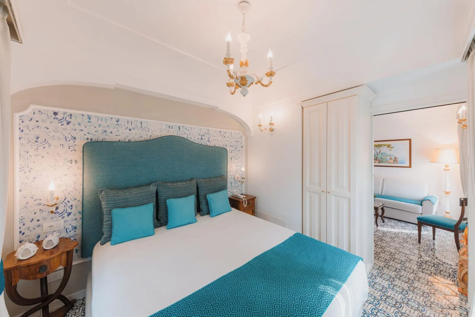 Prestige Suite FIORDALISO at Palazzo Pascal: a double bed with a teal headboard and a doorway through to a sitting room