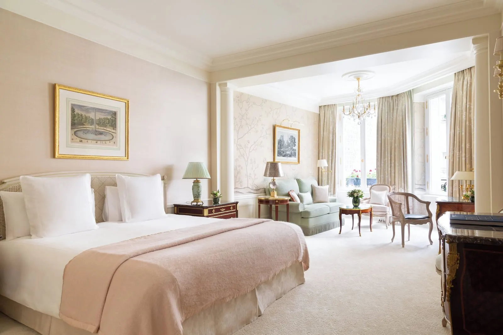 Suite Impériale at Le Bristol Paris: a bed with a blush throw and a sitting area beyond a pair of columns, with painted wallpaper and tall windows