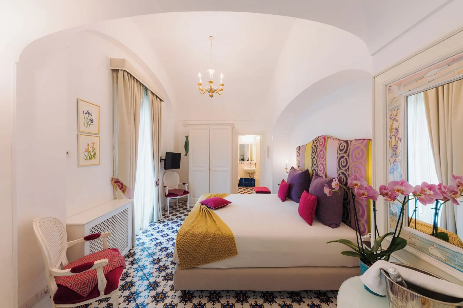 Superior Suite IRIS at Palazzo Pascal: a double bed with a striped headboard under a vaulted ceiling, a chandelier and a long window with curtains