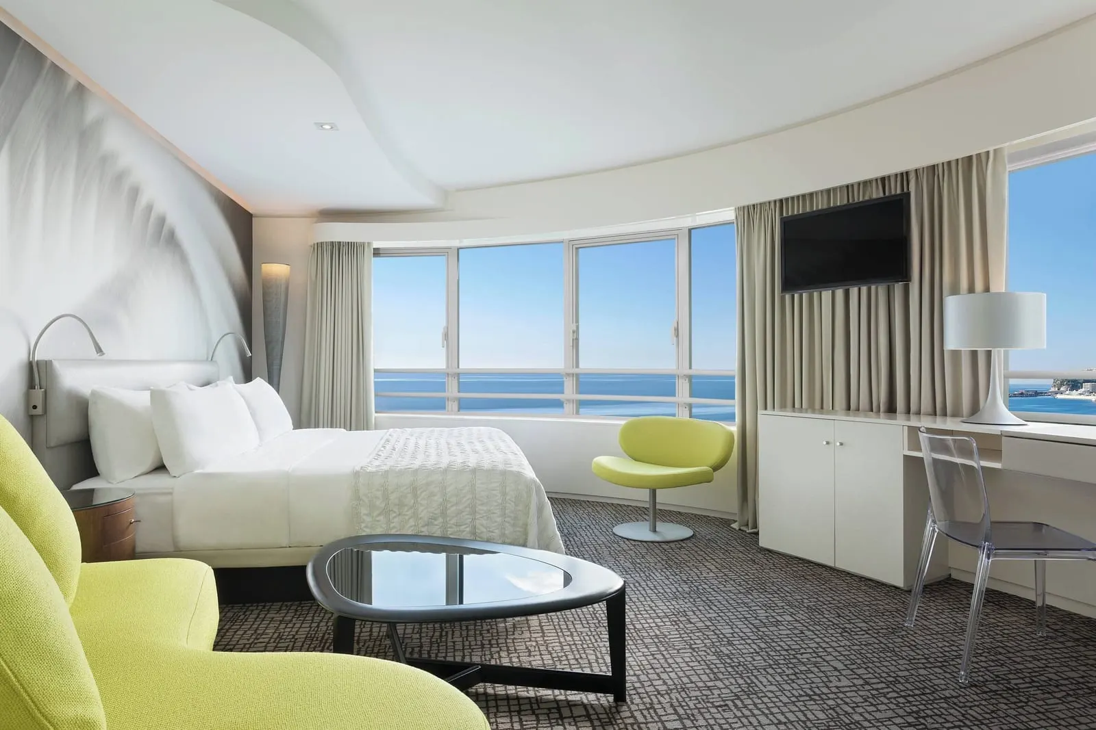 Design room at Le Méridien Beach Plaza: the bed, a lime-green armchair and curved windows onto the sea