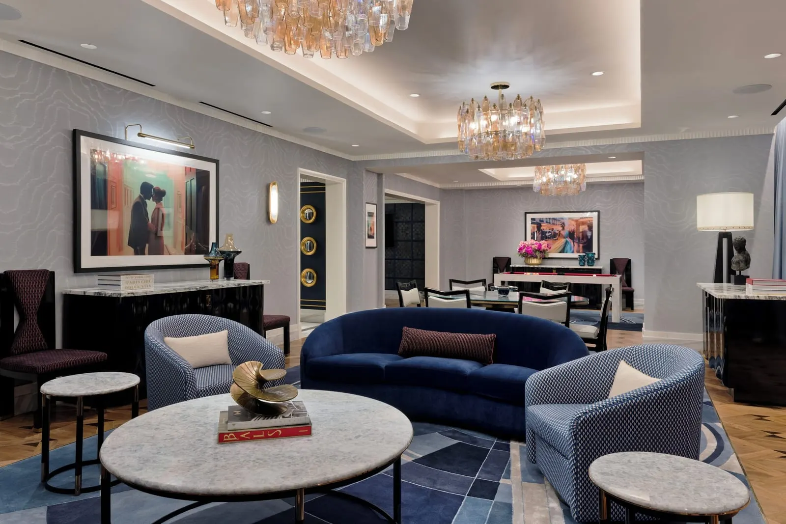 Fleur de Lis Crown Penthouse at Fontainebleau Las Vegas: the living room, with a curved navy velvet sofa and two patterned armchairs around a round marble table, and a dining table and a billiard table beyond