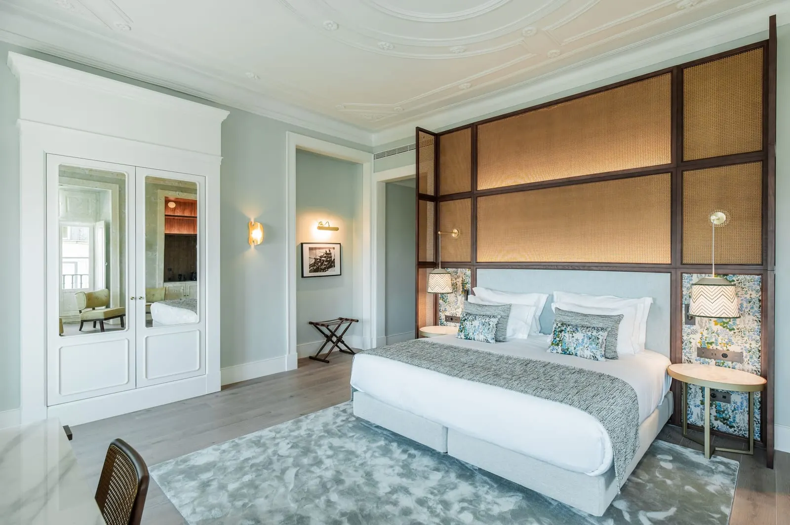 Deluxe Room at Palácio Ludovice: the bed under a tall rattan-panelled headboard, a stucco ceiling and mirrored wardrobe doors