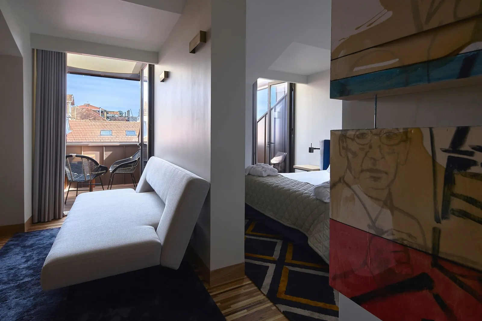 Superior Suite at Torel Avantgarde: a white chaise by the open balcony door, with the bed beyond a painted panel