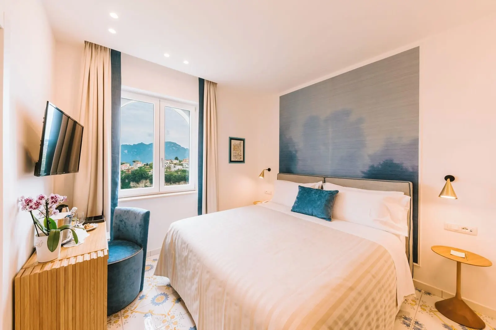 Classic Room RIBES at Palazzo Pascal: a double bed with a blue painted headboard panel, a blue armchair and a window onto the hills