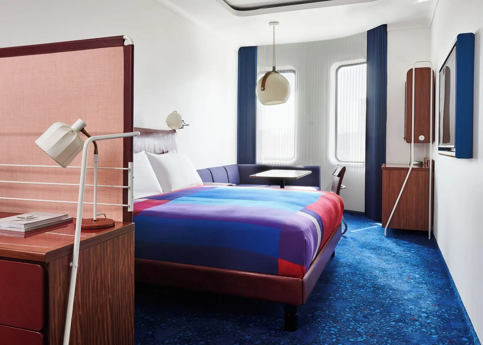 Deluxe King at The Standard, London: the bed with a striped blanket, a pink screen, a desk lamp and a navy sofa