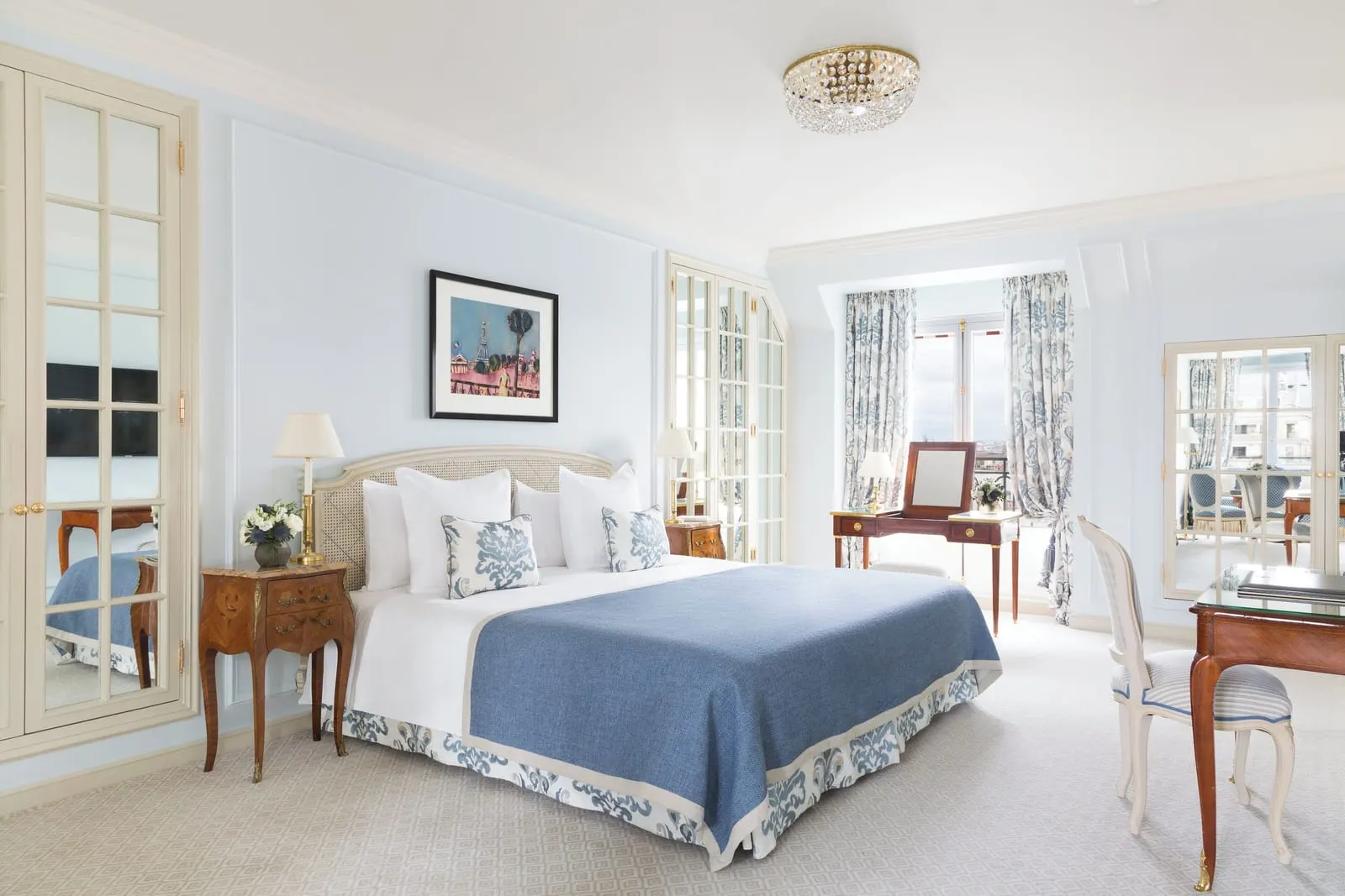 Junior Suite with balcony at Le Bristol Paris: a bed with a blue throw and damask cushions, a dressing table in the window bay and mirrored wardrobe doors