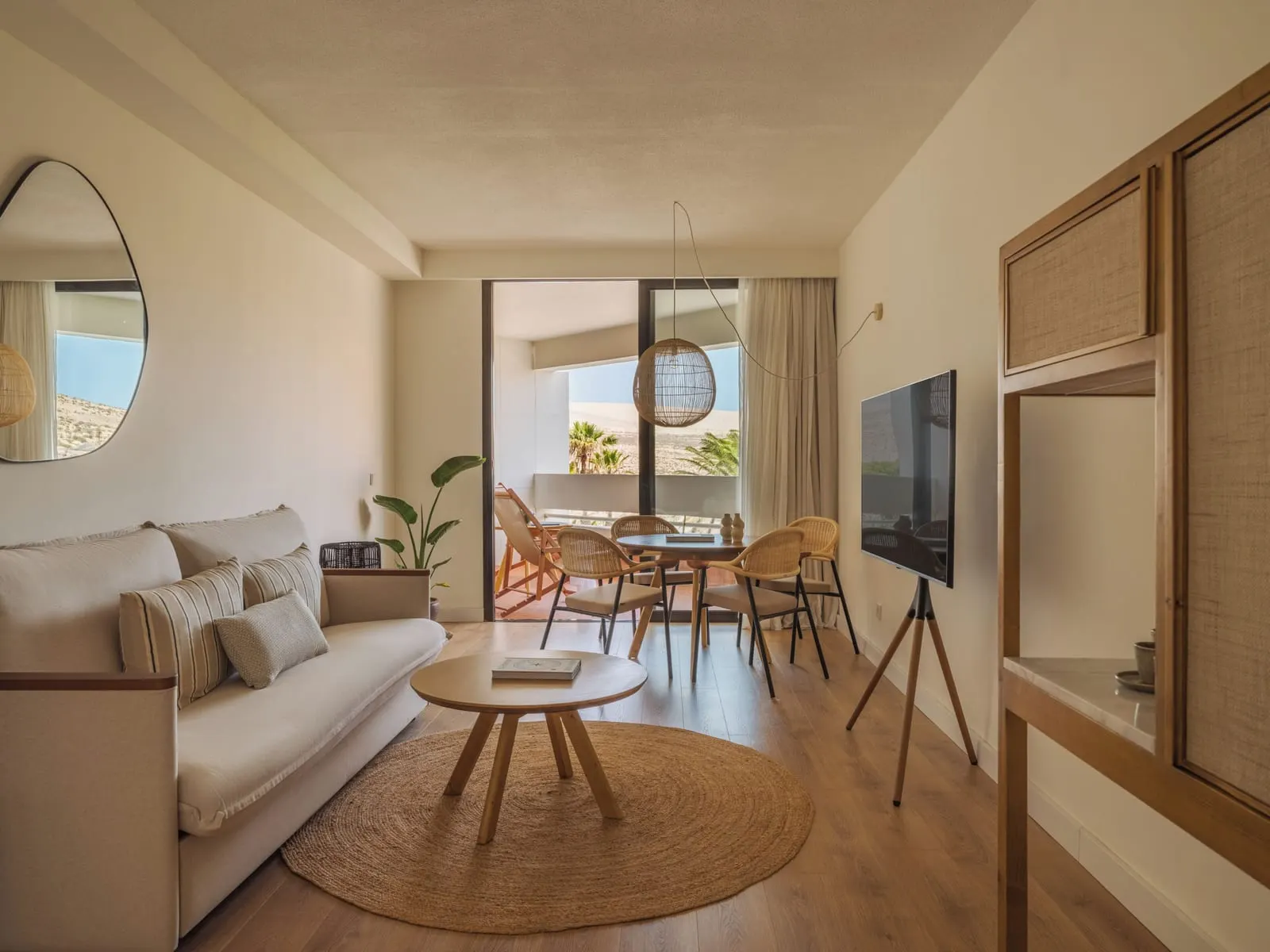 Suite at Paradisus by Meliá Fuerteventura: a living room with a sofa, a round coffee table, a television on a stand and a dining table for four by the terrace door