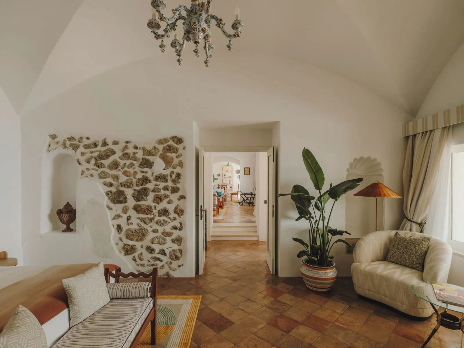 Divina Signature Suite at Caruso, A Belmond Hotel: a vaulted living room with a section of bare stone wall, a sofa, an armchair and a terracotta floor leading through to further rooms