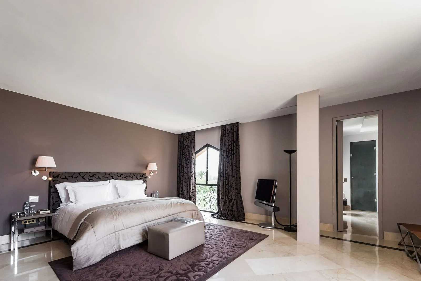 Lounge Suite at Palais Namaskar: a king bed on a patterned rug with an arched window and a doorway through to the bathroom