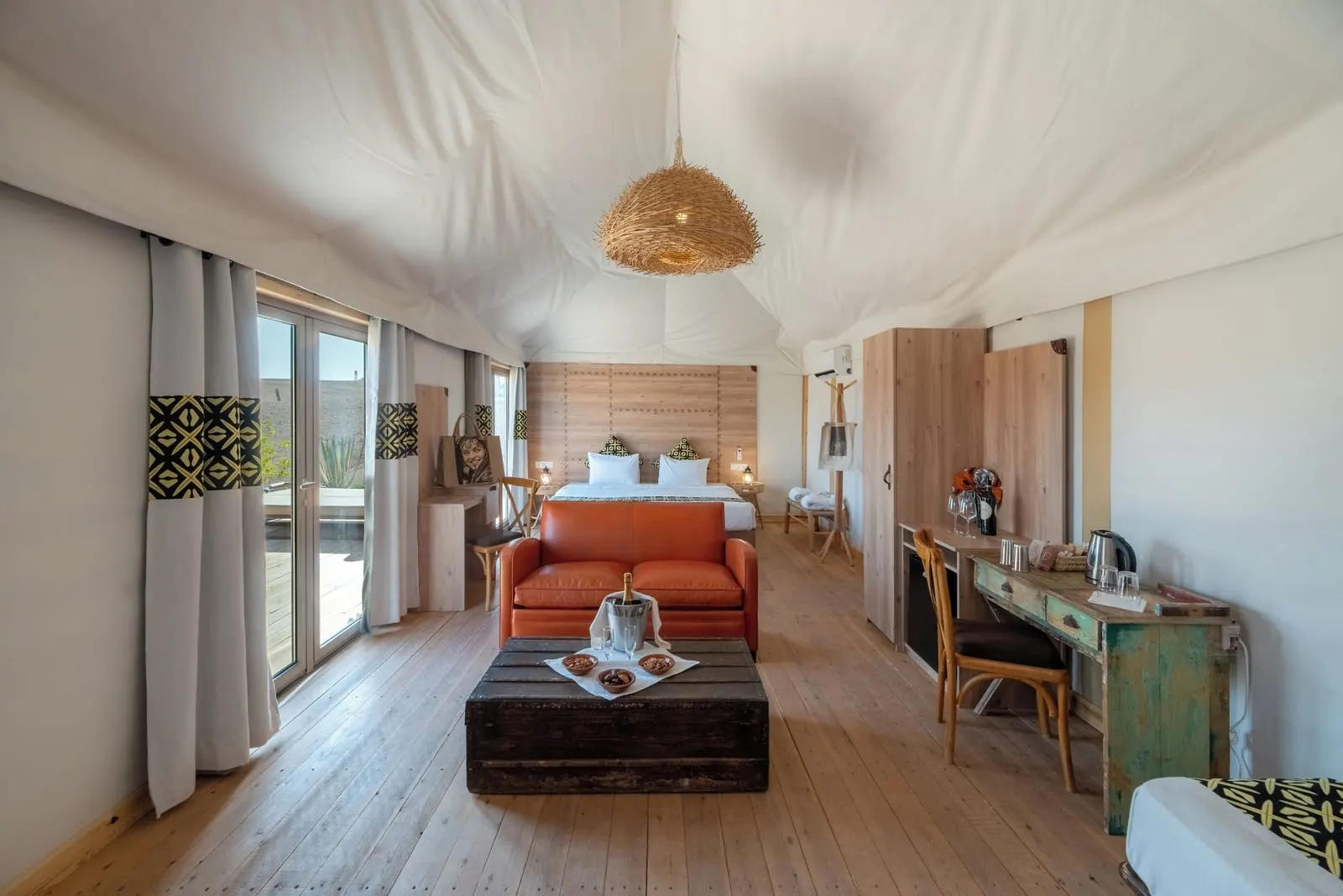 Inara Suite at Inara Camp: a long open room with an orange sofa and a low wooden chest in front, a desk to one side and the bed at the far end.