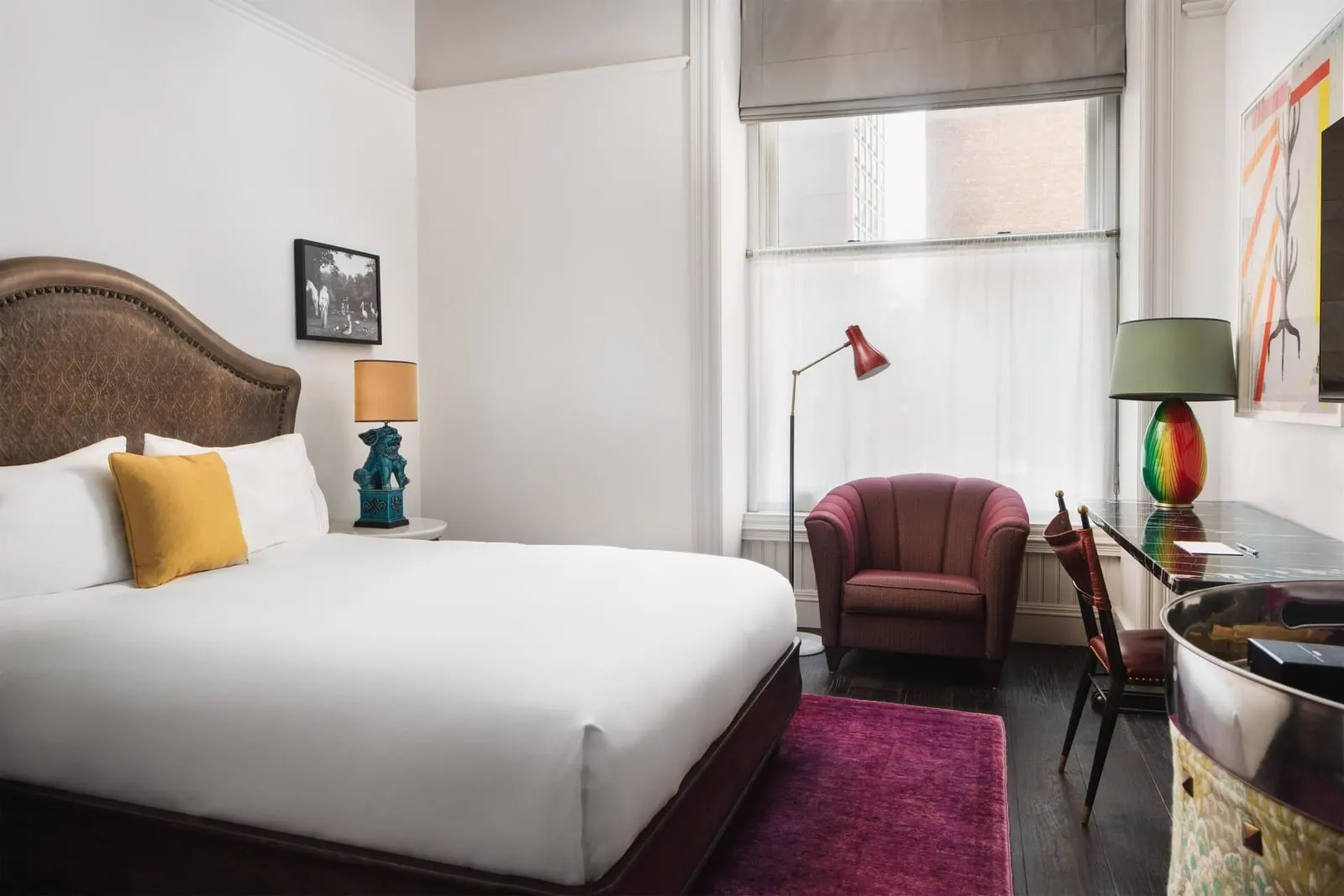 Superior Queen at The Beekman: a queen bed with a studded leather headboard, a burgundy armchair beside a tall window and a dark marble desk with a coloured glass lamp