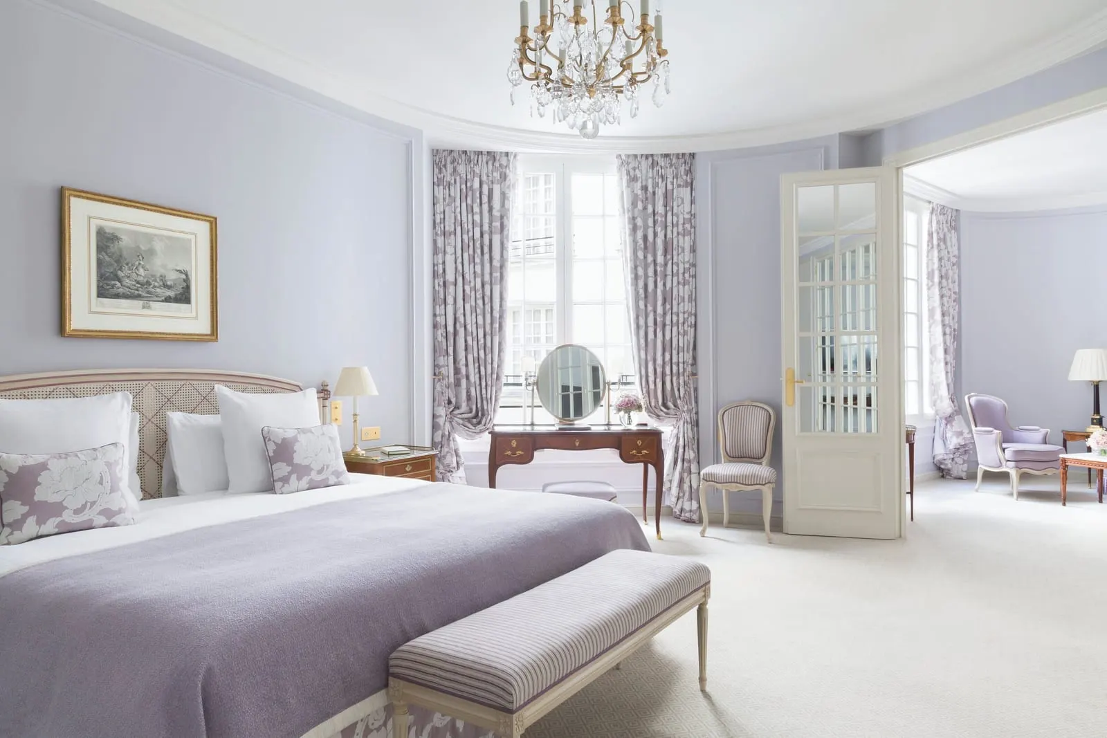 Prestige Junior Suite at Le Bristol Paris: a bed with a lilac throw, a dressing table between the windows and a glazed door open to the sitting room