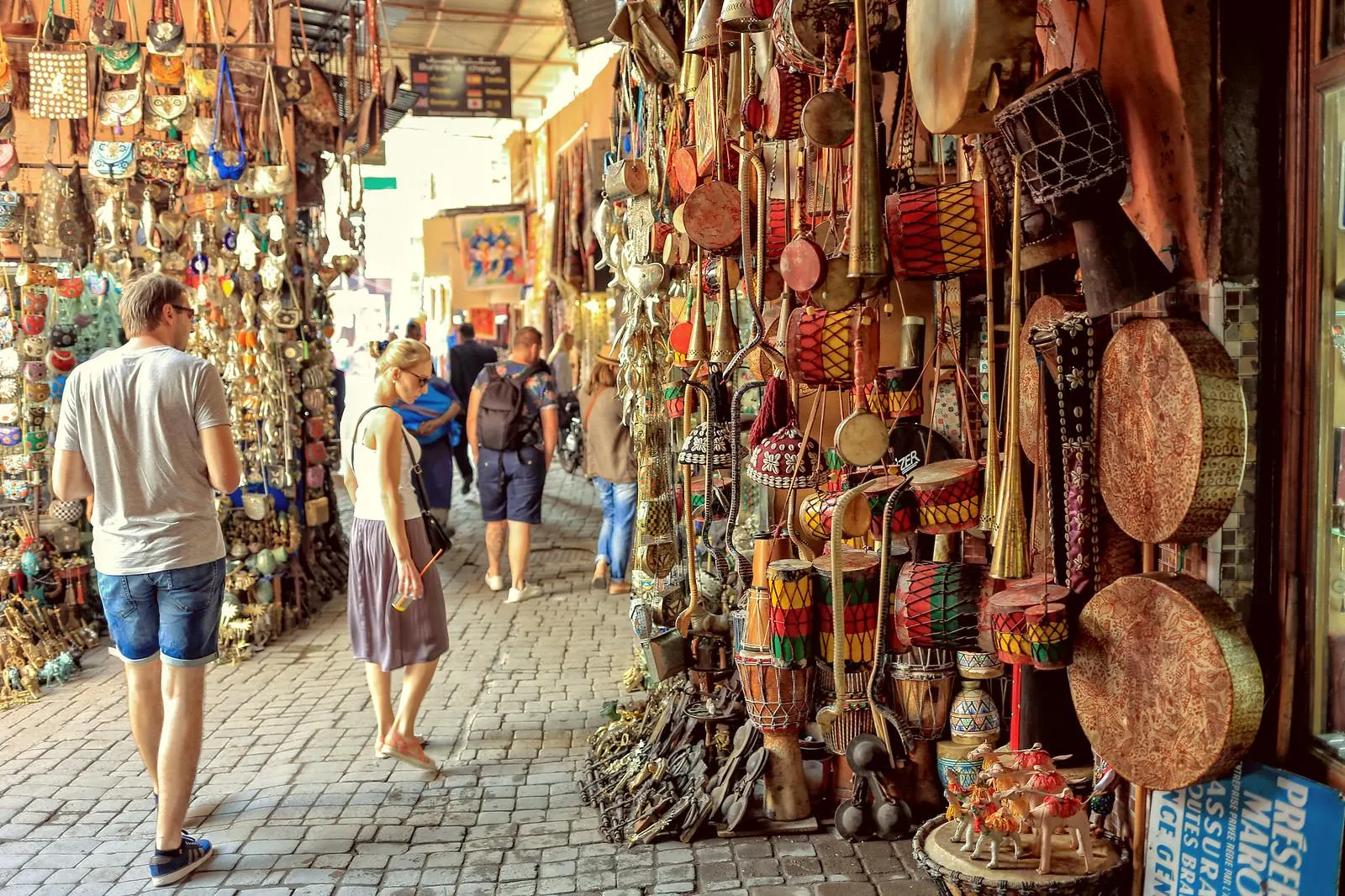 Visitors walking through a souk lane lined with lanterns, drums and metalwork