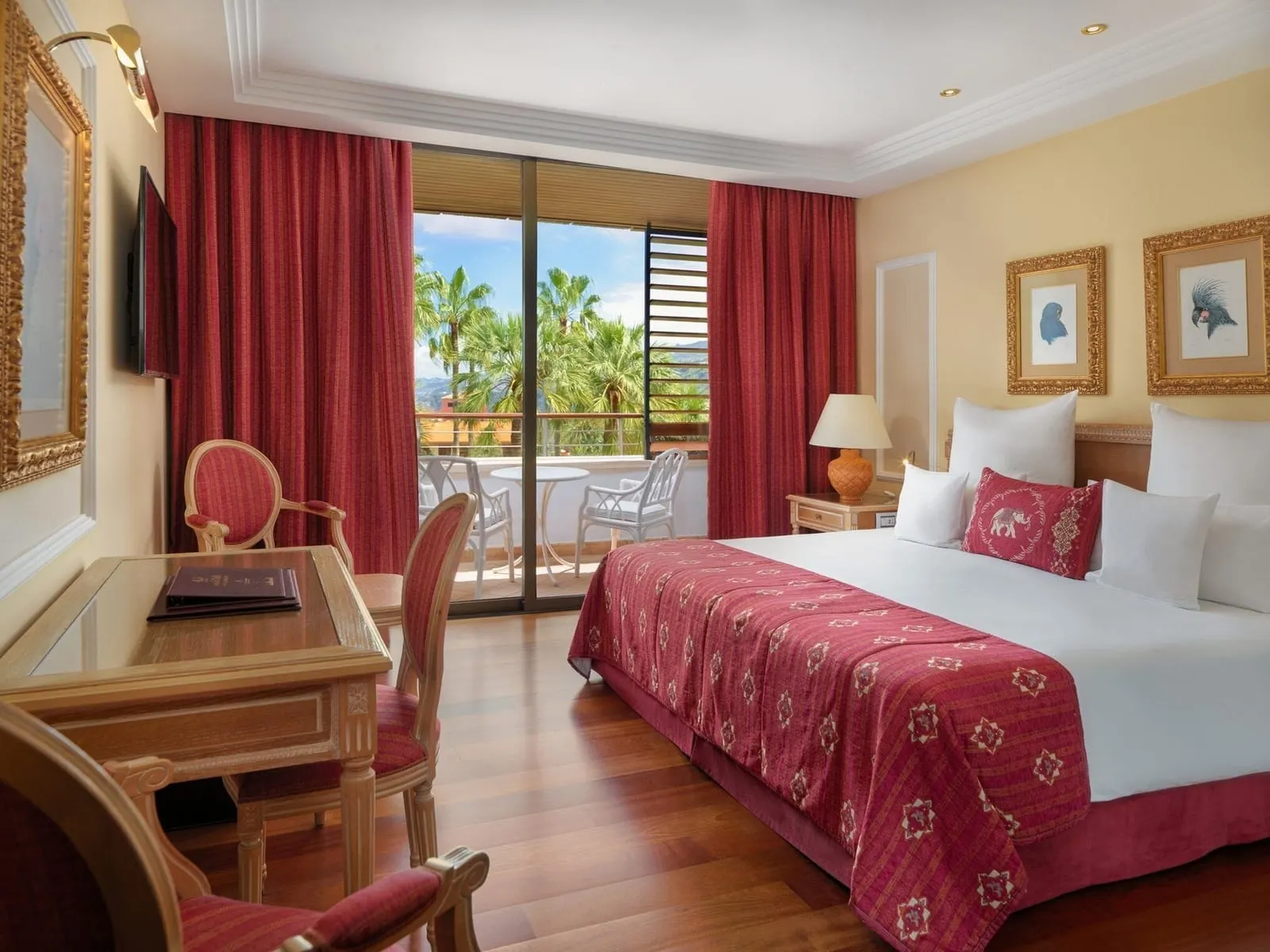 Deluxe Garden View at Hotel Botánico: a king bed with a red bedspread, a desk and a balcony door onto palms