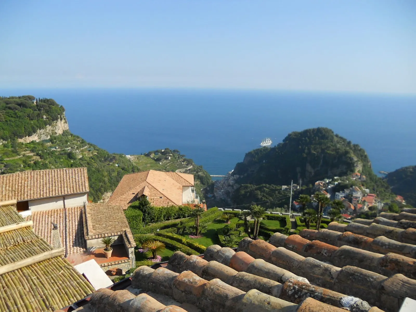 Deluxe Suite EDERA at Palazzo Pascal: a view over tiled roofs and a terraced garden down to a wooded headland and the sea