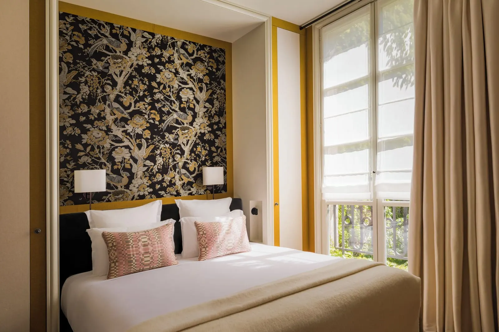 Superior Room at Le Pavillon de la Reine: a double bed against a bird and blossom panel, beside a tall window with a low iron railing