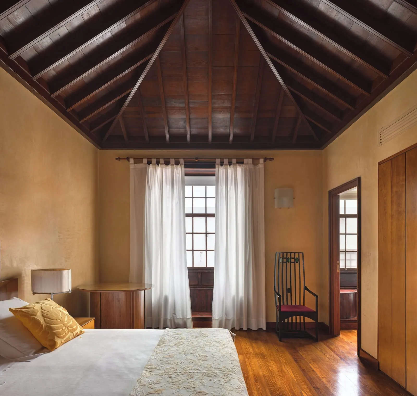 Double Superior at Hotel San Roque: a bed under a pitched timber ceiling, ochre walls and a tall window