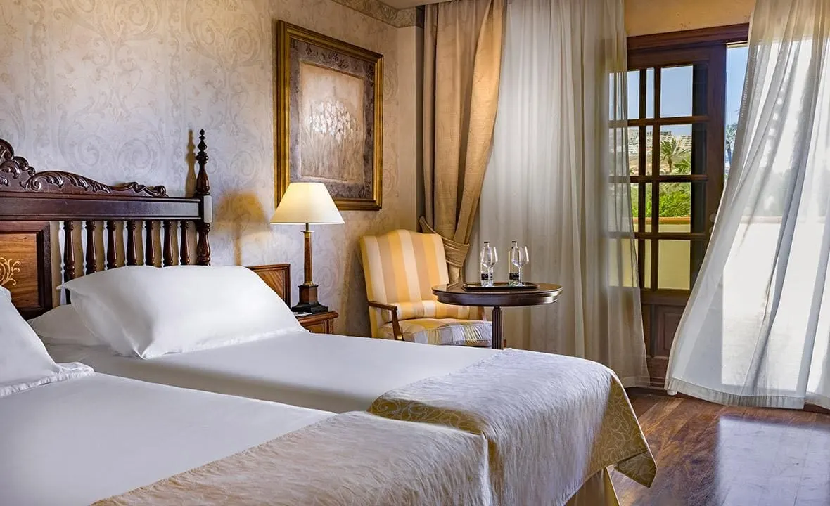 Deluxe double room with view of golf course at Elba Palace Golf Boutique Hotel: twin beds, an armchair and a small table beside a glazed balcony door