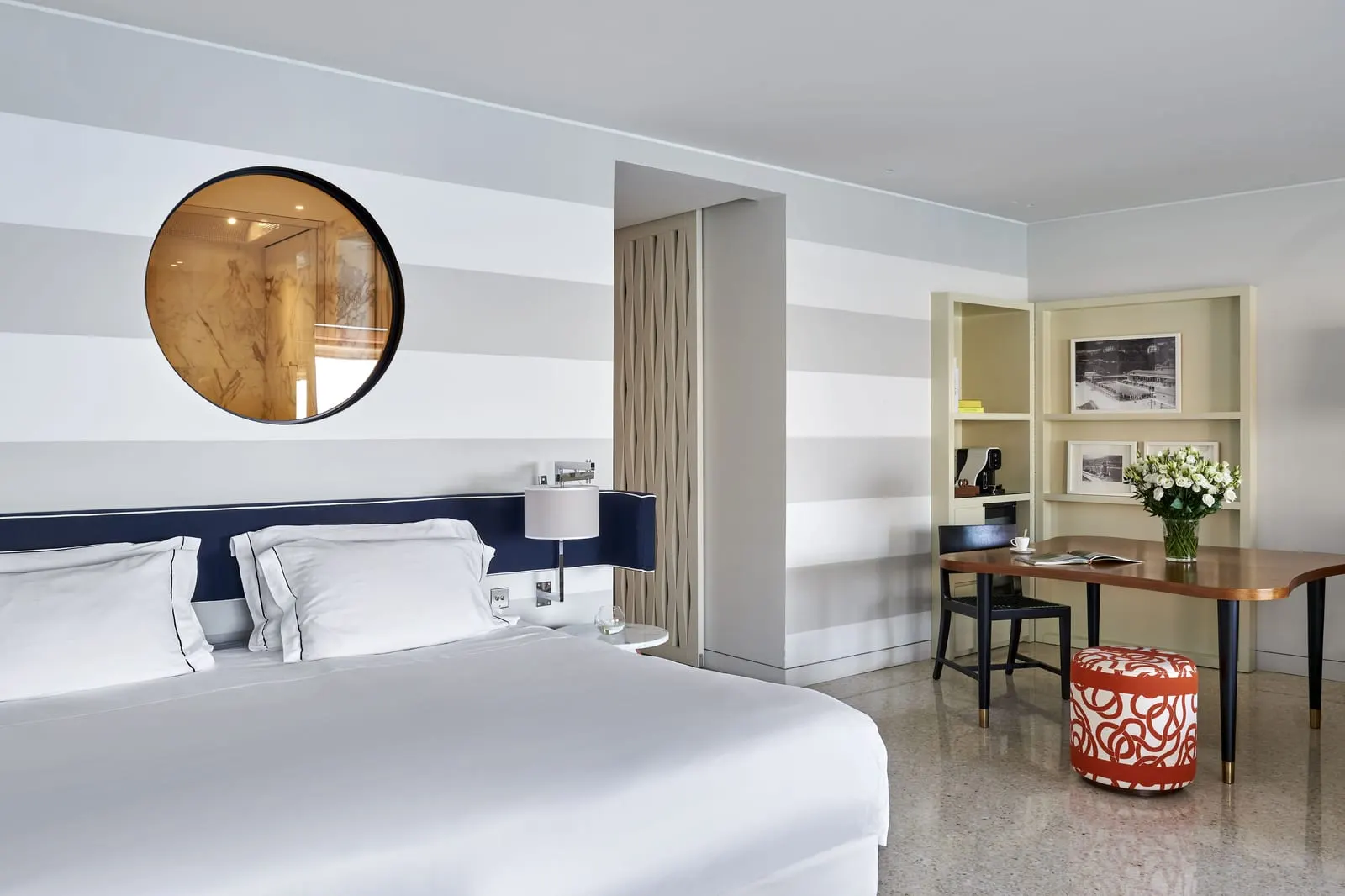 Loft Suite at Monte-Carlo Beach: the bed below a round porthole, with a desk and shelves in the corner