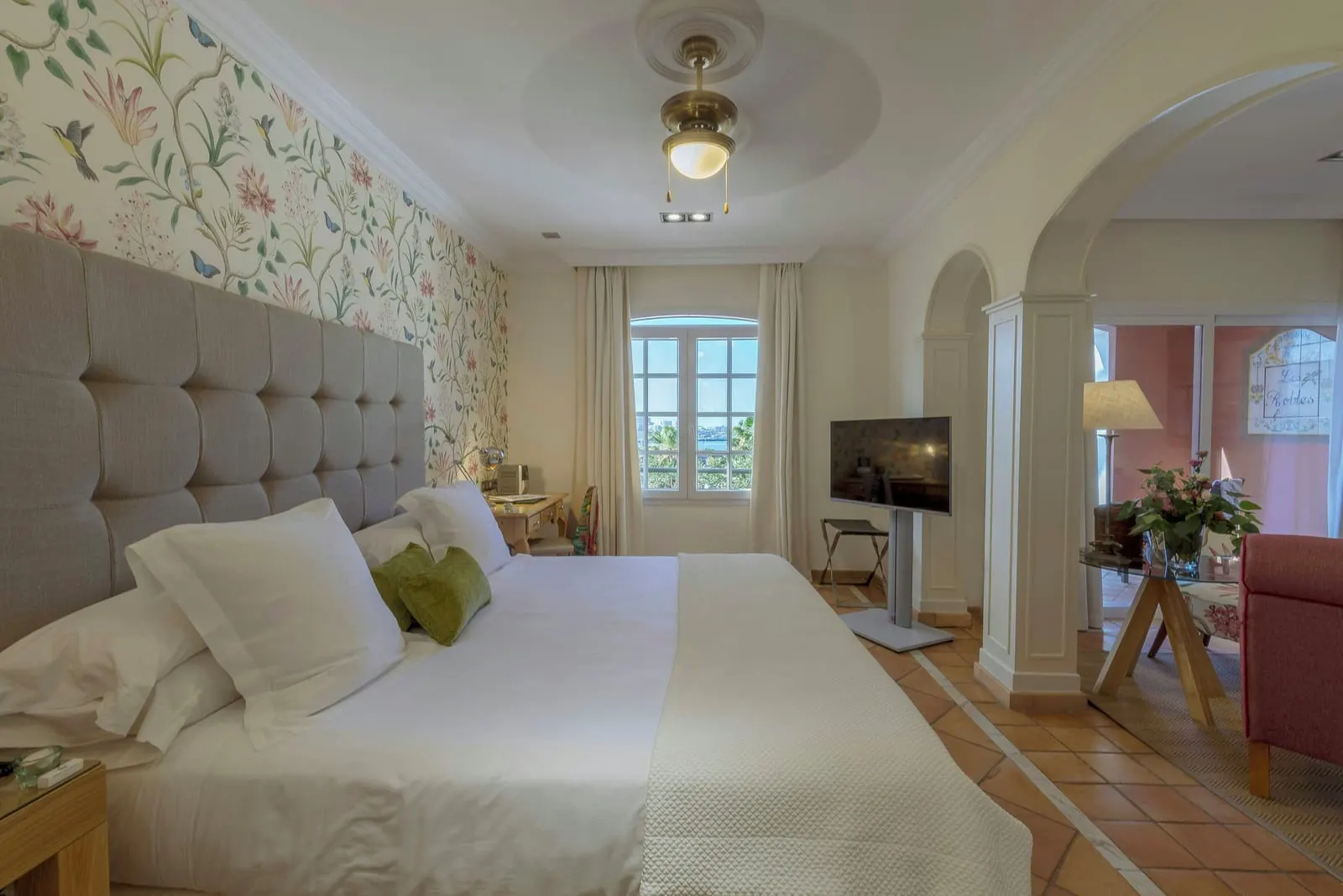Casas Ducales Junior Suite at Bahía del Duque: the bed against floral wallpaper, with an arch through to the sitting area