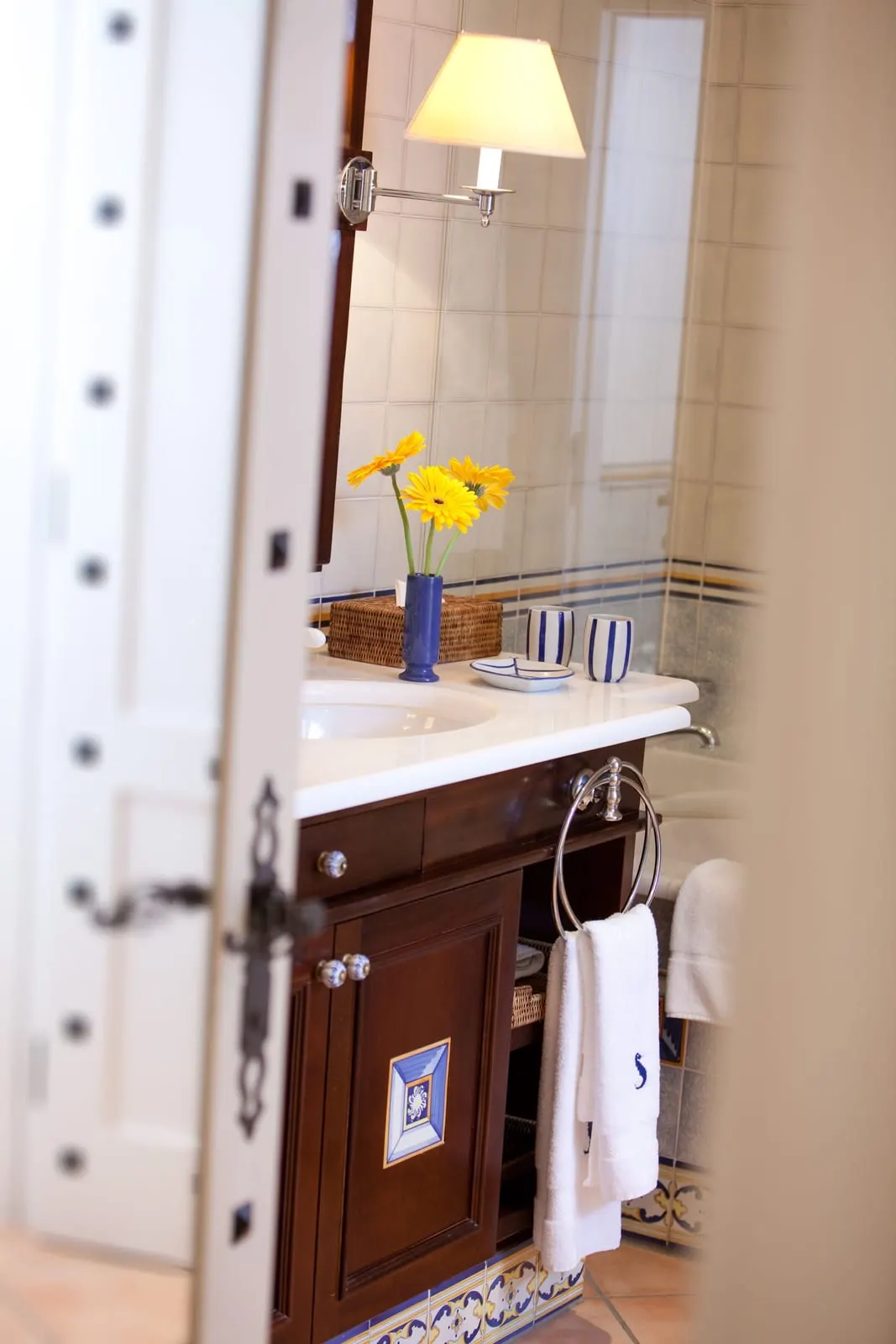 Junior Suite at Seaside Grand Hotel Residencia: a basin in a dark wood vanity with a wall lamp and yellow flowers, and a bath behind, seen through the bathroom door