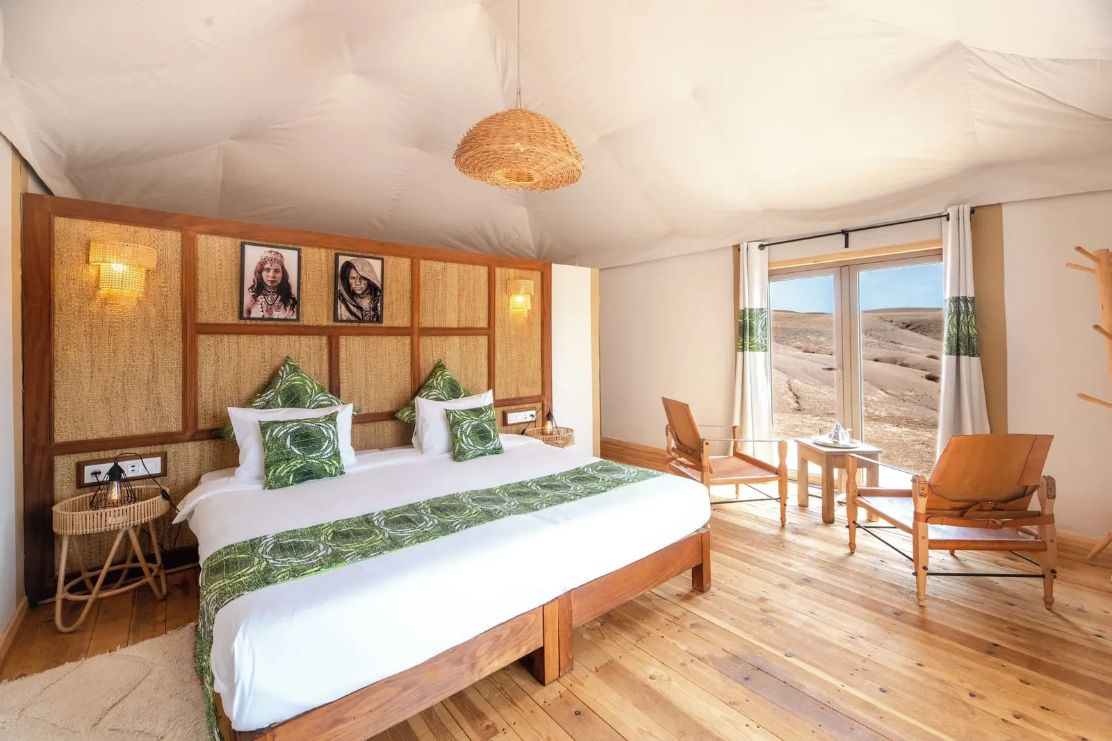 Agafay Suite at Inara Camp: a king-size bed with green cushions against a woven headboard, with two armchairs by glass doors.