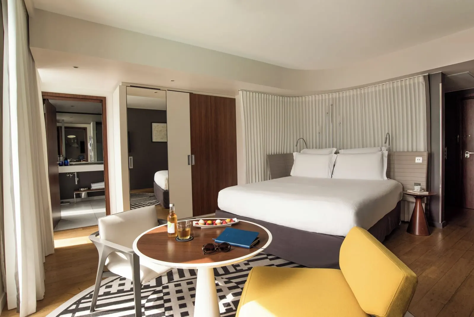 Executive Room at Hôtel Molitor Paris: a king-size bed, a round table with a yellow armchair on a patterned rug, and the bathroom door open beyond