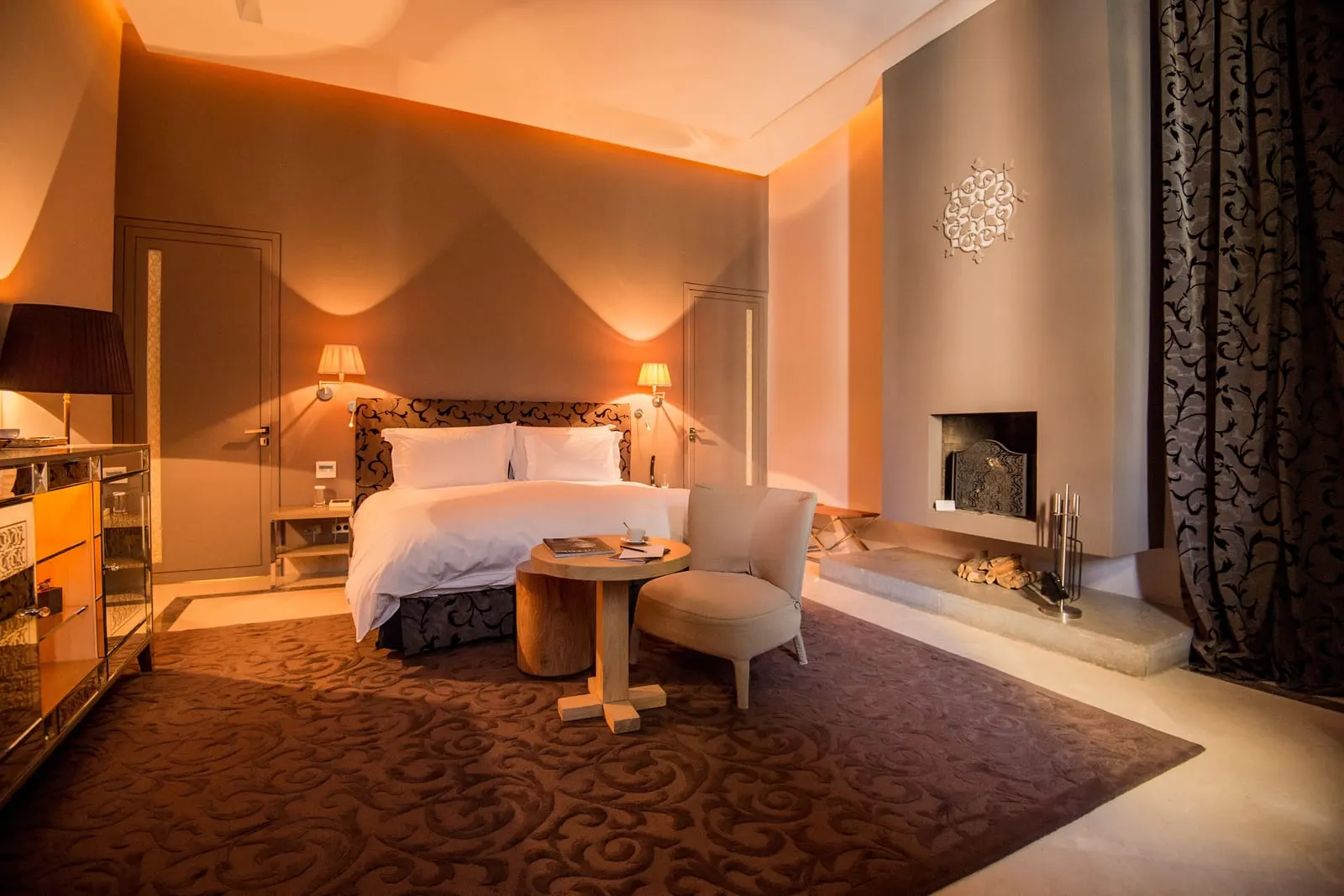 Pool Palace at Palais Namaskar: a warmly lit bedroom with a king bed, a fireplace and a small round table
