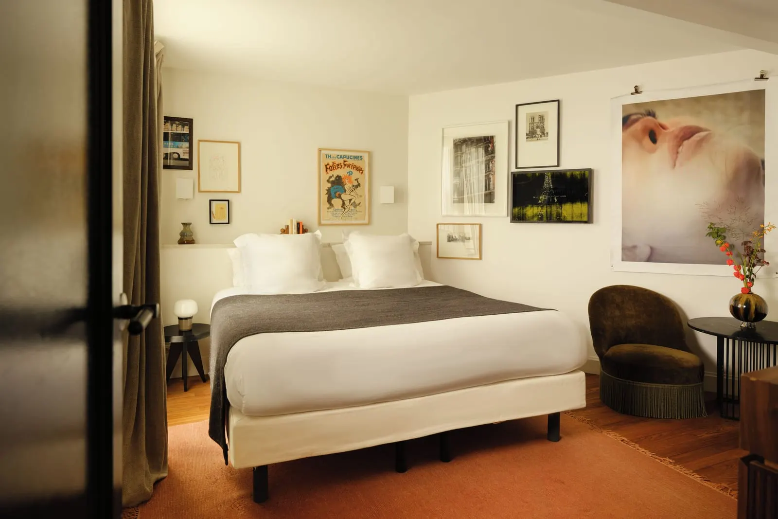 Pigalle 21 at Le Pigalle: a double bed under a wall of framed prints and posters and a large photographic portrait, with a fringed velvet armchair and a small round side table