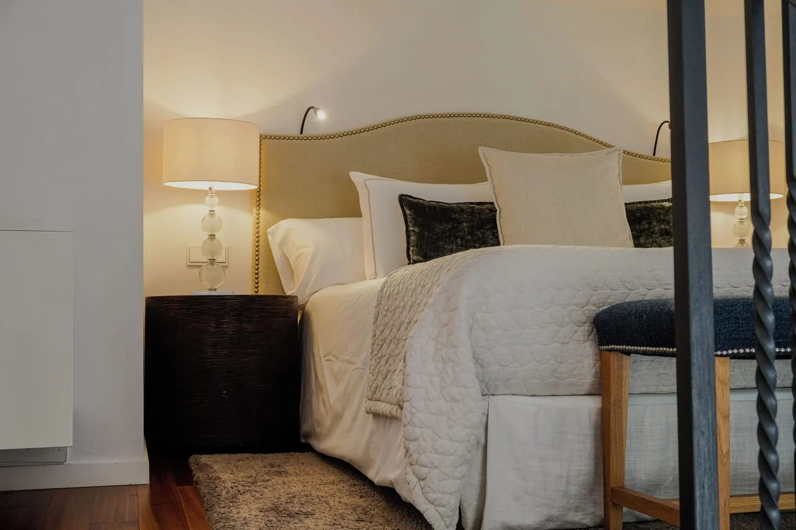 Double Room Duplex at L'Avenida Hotel: a double bed with a tall upholstered headboard beside a twisted iron stair balustrade