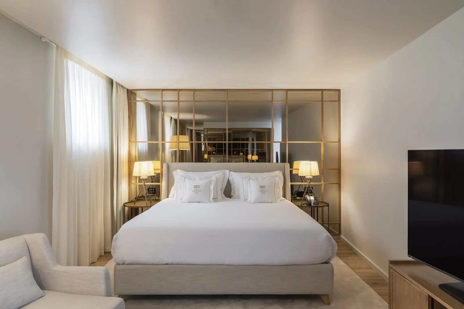 King Suite Sé Cathedral View Balcony at Casa da Companhia: the bed against a brass-framed mirror wall, a television and an armchair