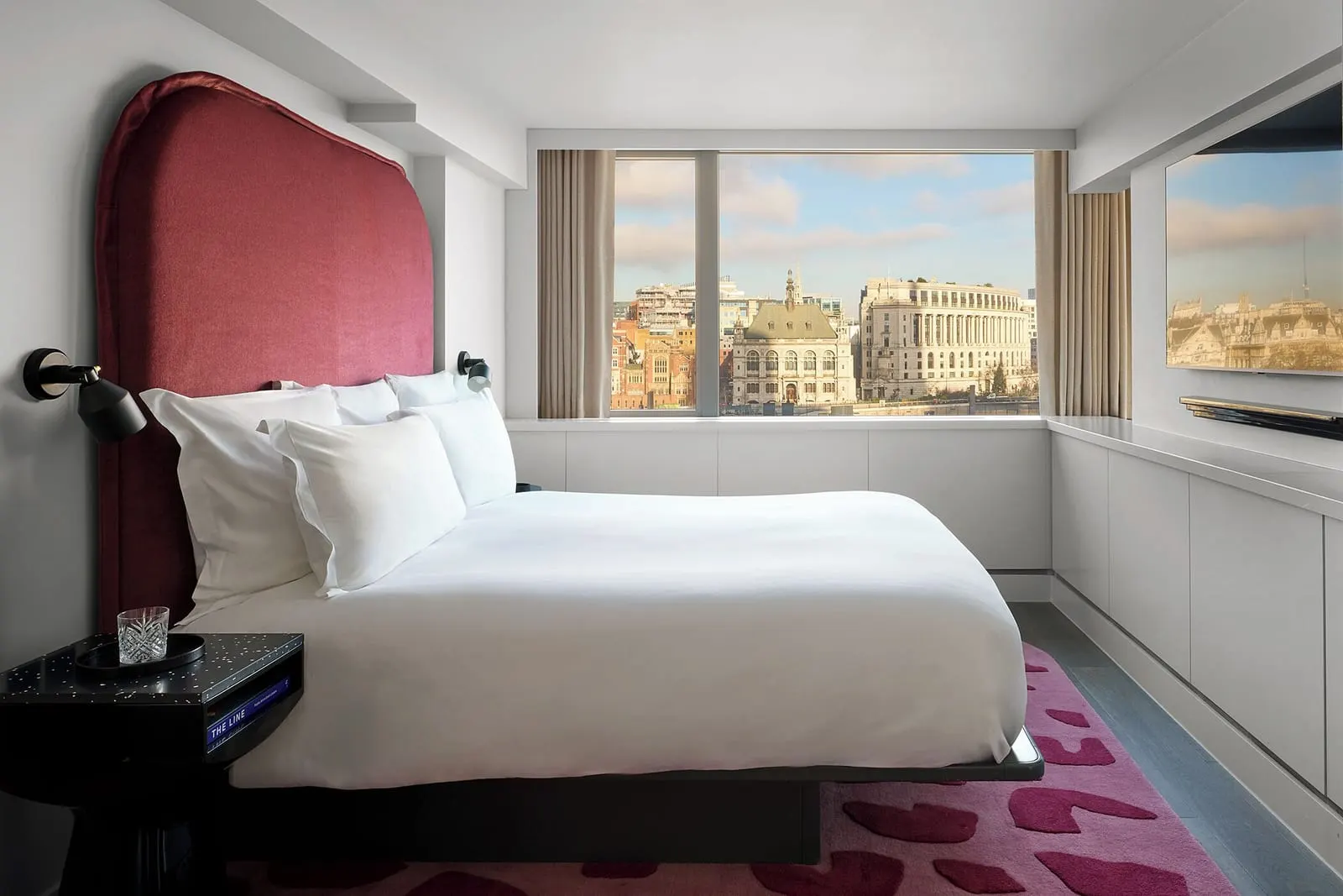 Riverview One Bedroom Suite at Sea Containers London: the bed with a red headboard and a wide window onto stone buildings