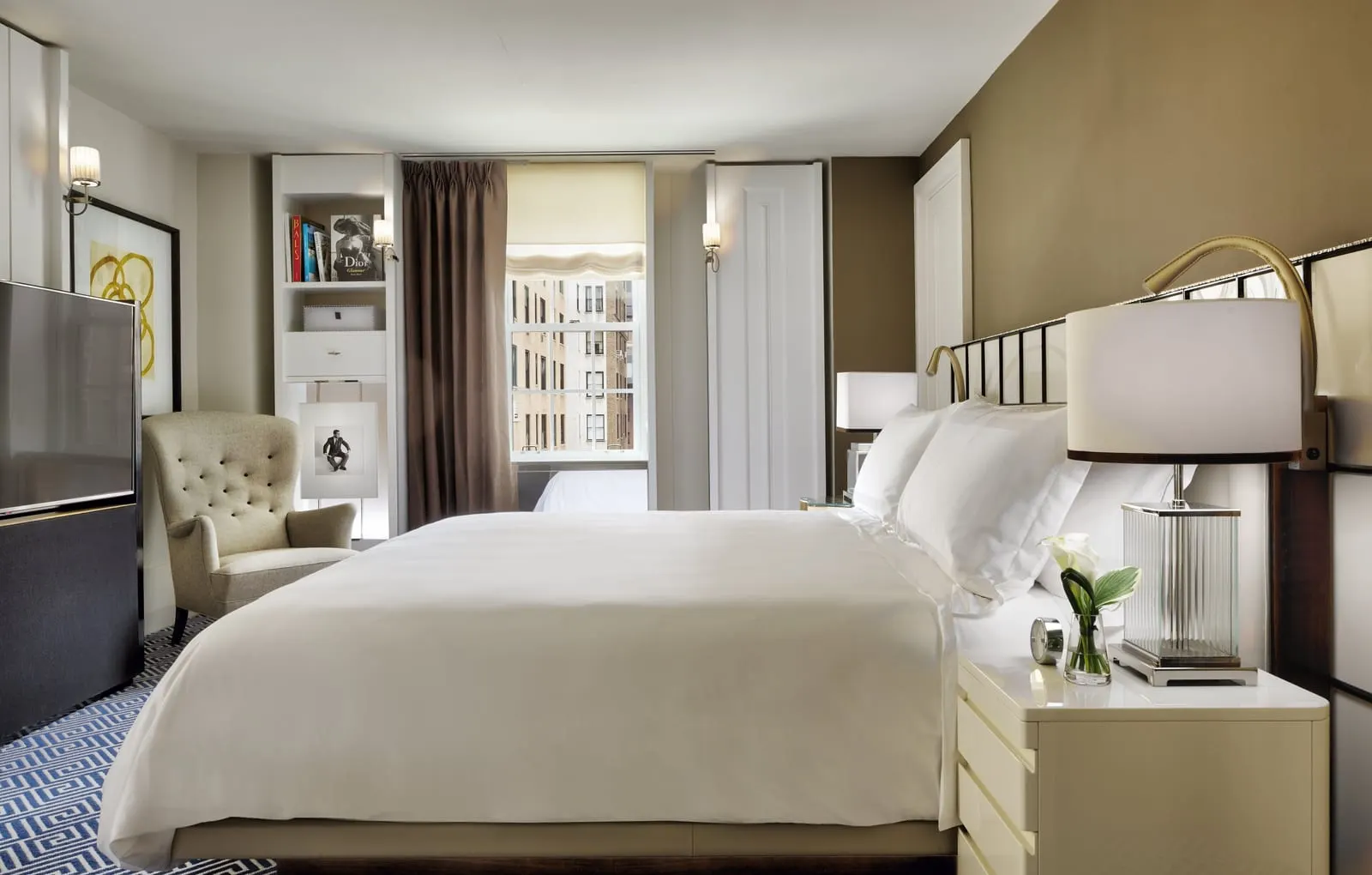Superior Two-Bedroom Suite at The Carlyle: a king bed beside a white bedside chest, with an armchair, a bookshelf and a television