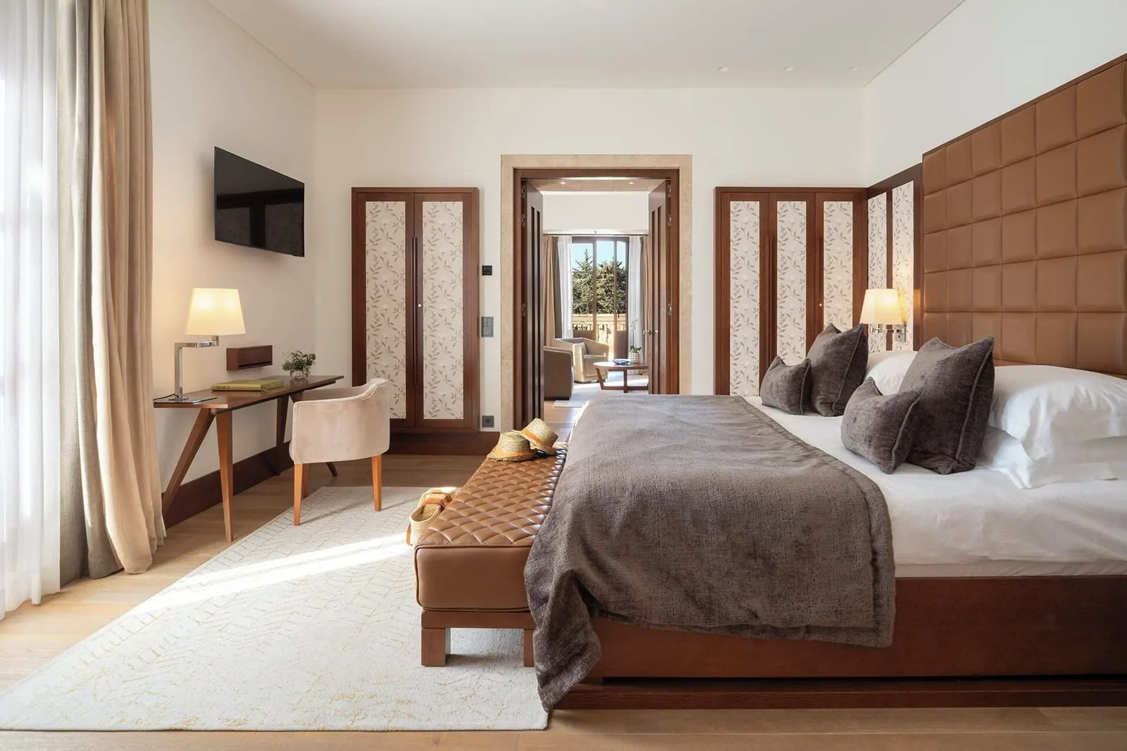 Tower Suite im Castell Son Claret: ein Schlafzimmer mit einem hohen gesteppten Kopfteil, einer Lederbank, einem Schreibtisch und einem Sessel und ein Durchgang zu einem Wohnzimmer