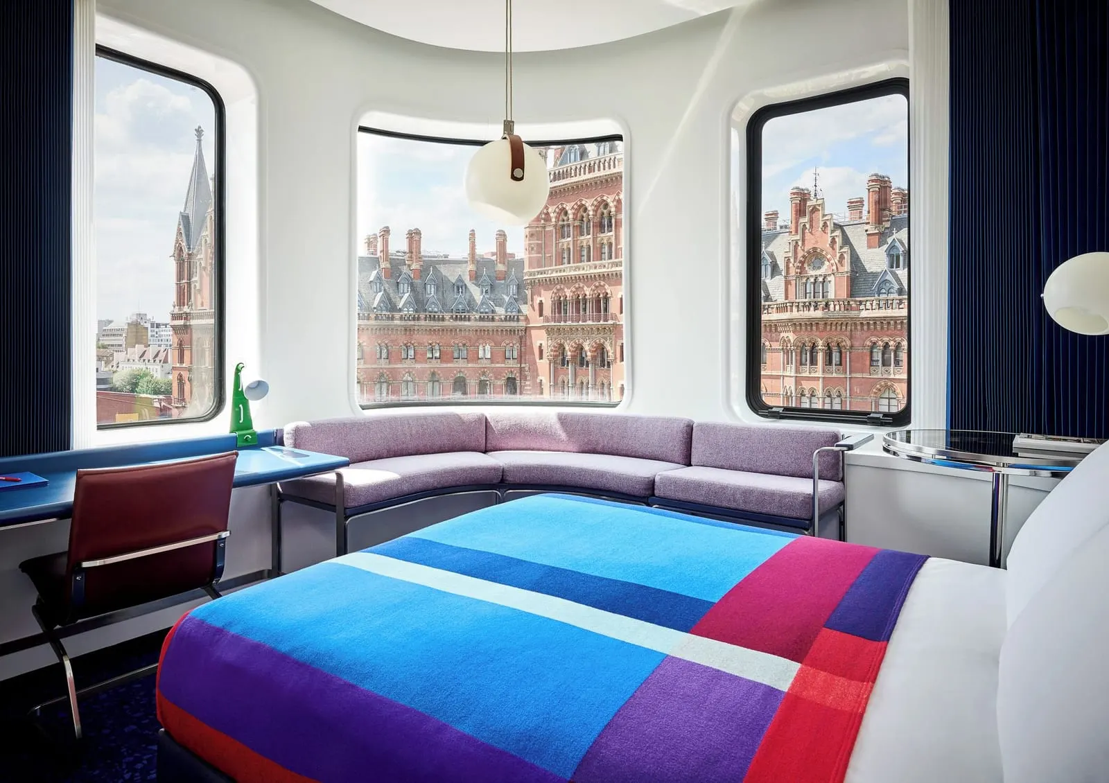 Deluxe Queen at The Standard, London: the bed with a striped blanket and a lilac sofa in a bay of round-cornered windows