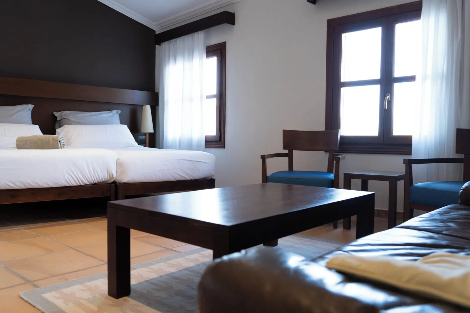 Junior Suite City at Maristel Hotel & Spa: twin beds with a dark wood headboard, a low coffee table, a leather sofa and two armchairs by a window