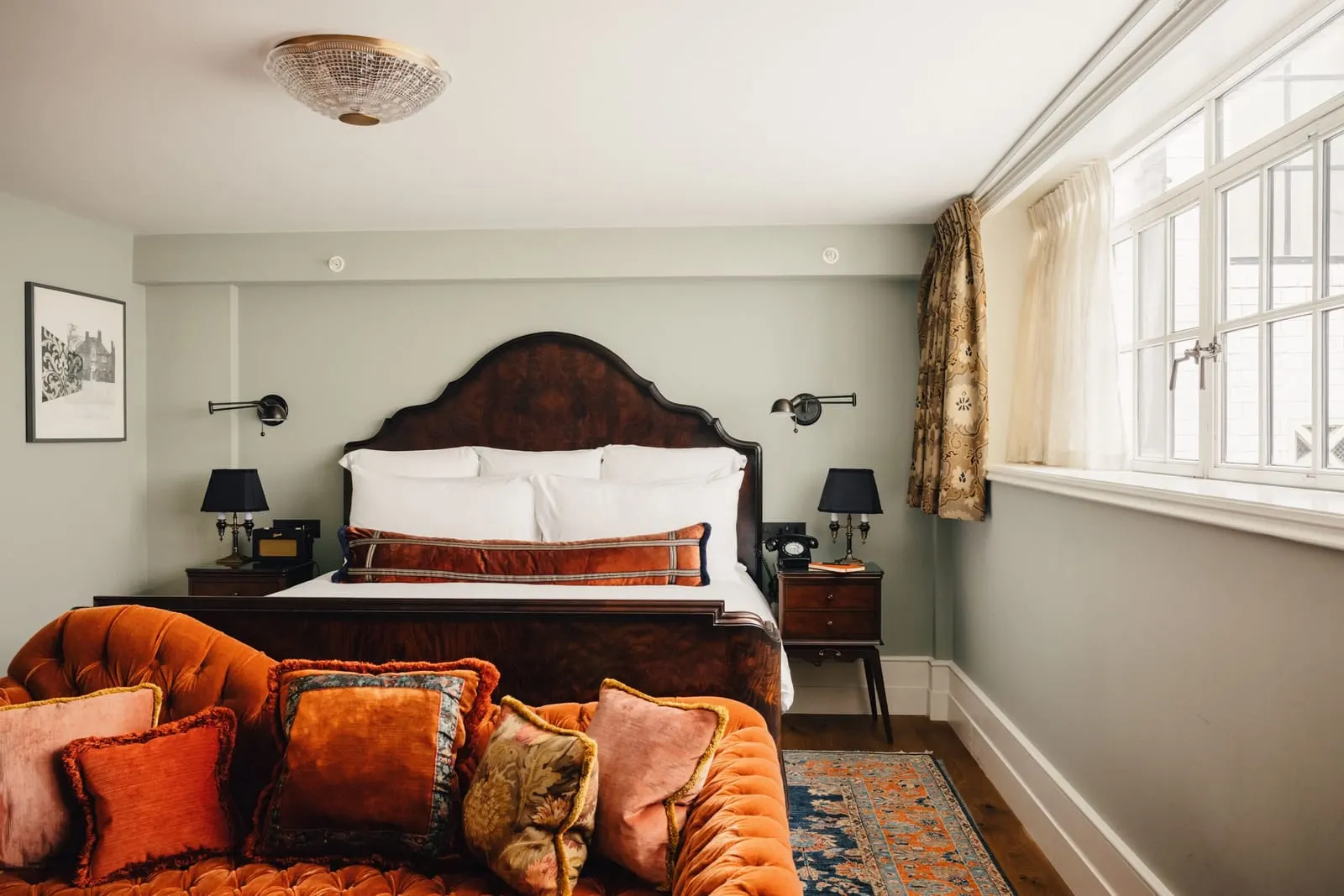 Stairwell Studio at The Ned: the bed with a carved headboard and an orange velvet sofa at its foot