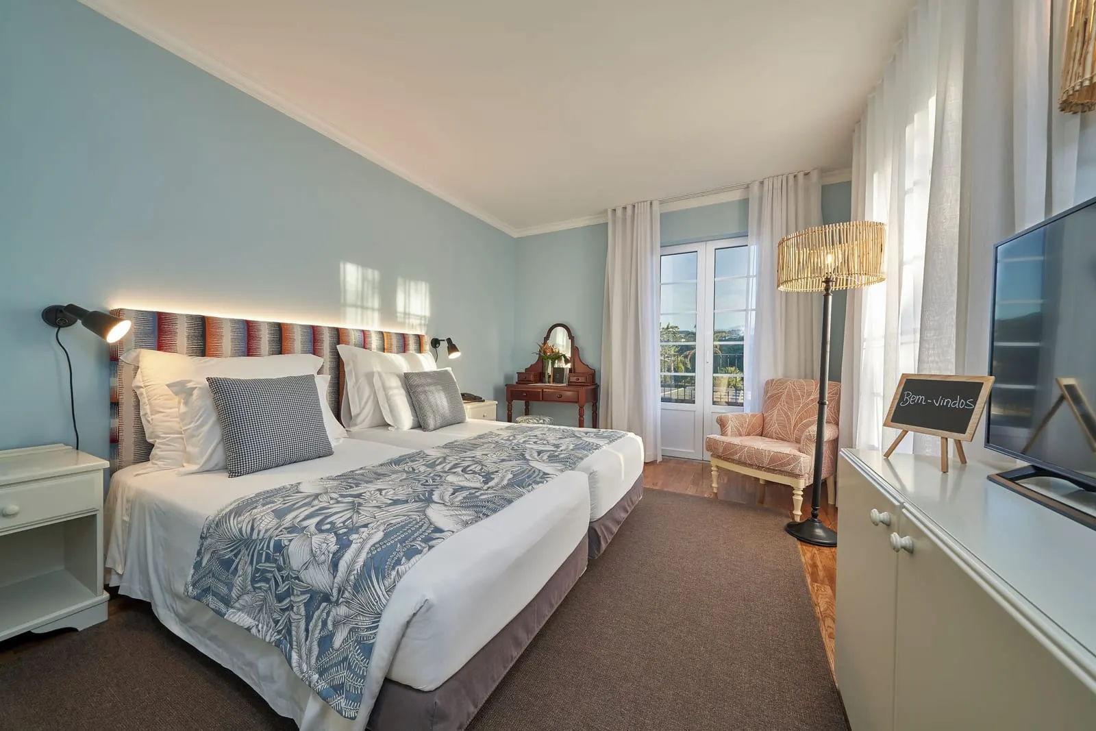 Classic at Hotel Quinta do Furão: two single beds made up as a double under a striped headboard, in a pale blue room with an armchair, a dressing table and a glazed door with white curtains