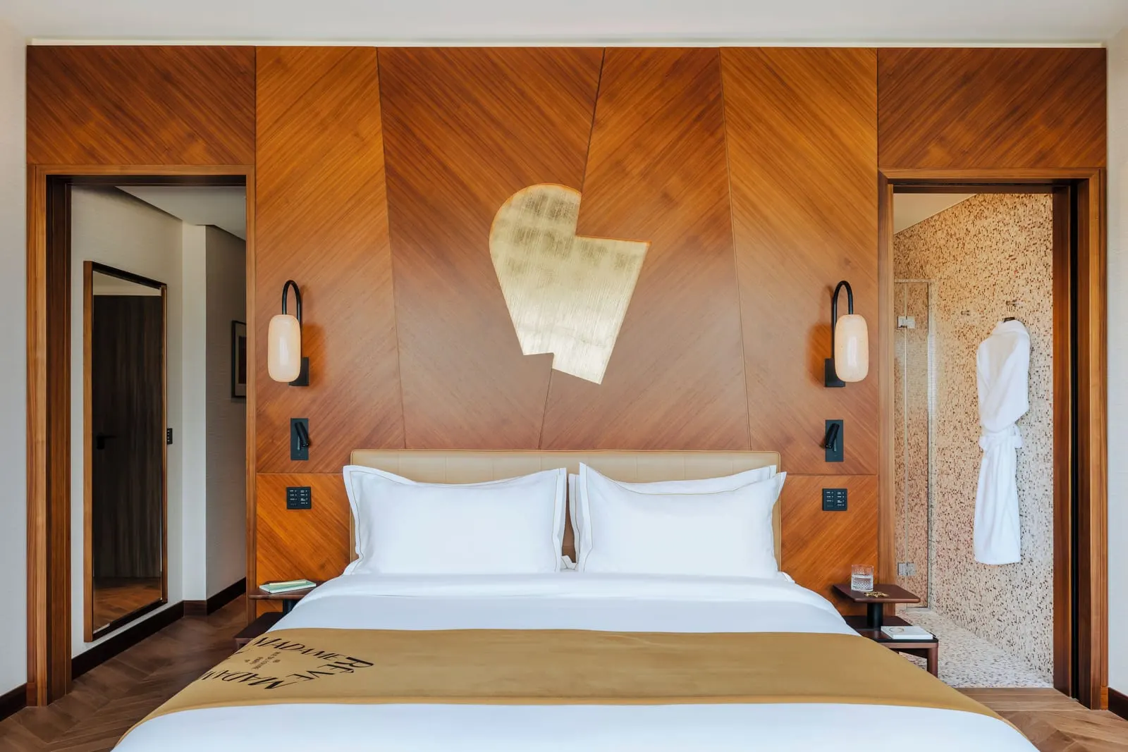 Deluxe Atelier at Hôtel Madame Rêve: a king bed against a walnut-panelled wall with a gold-leaf motif, between an open doorway with a full-length mirror and a mosaic-tiled shower room