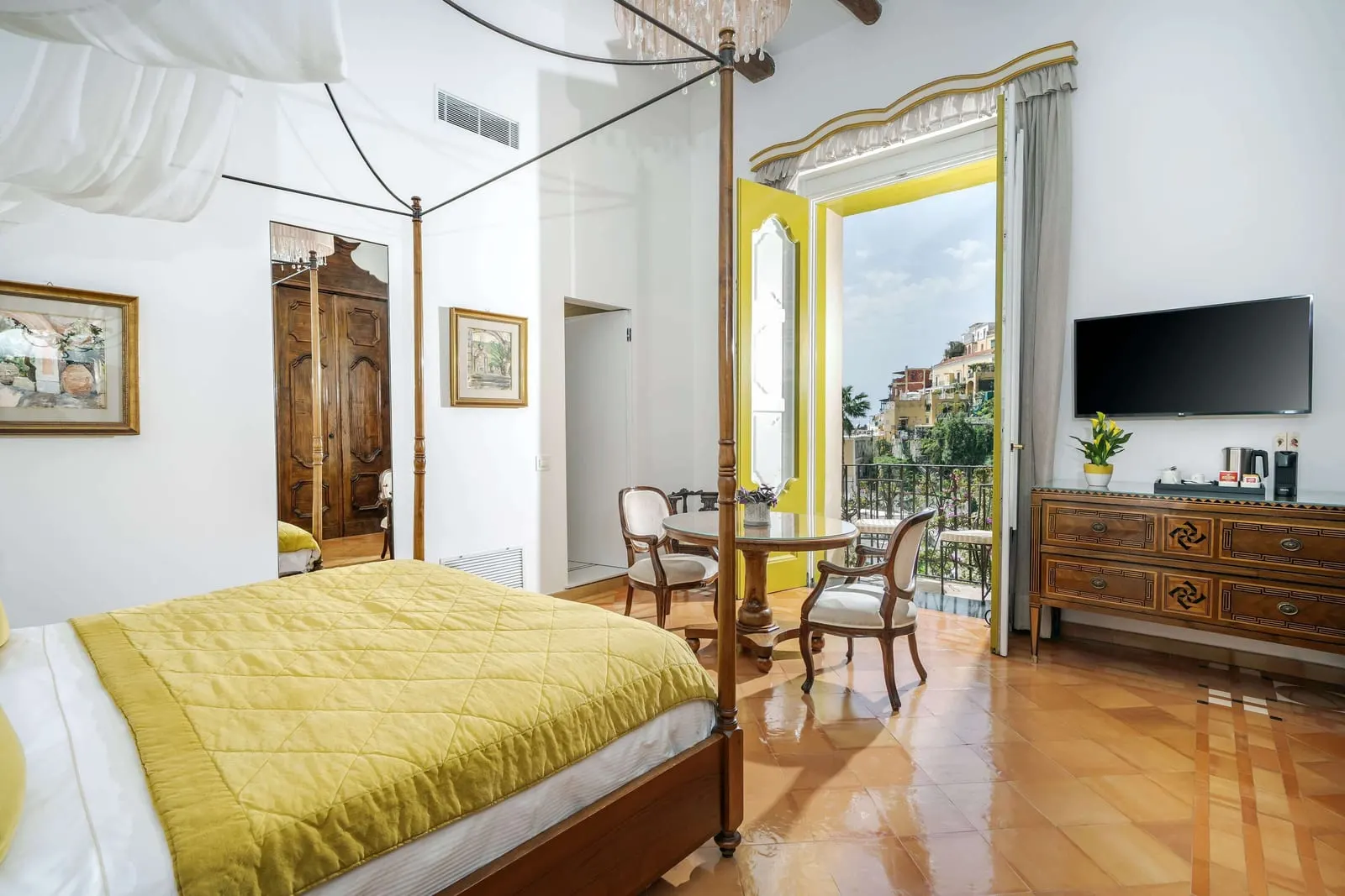 Deluxe Sea View im Palazzo Murat: ein Himmelbett mit gelber Decke, eine antike Kommode und ein kleiner Tisch an den geöffneten Balkontüren