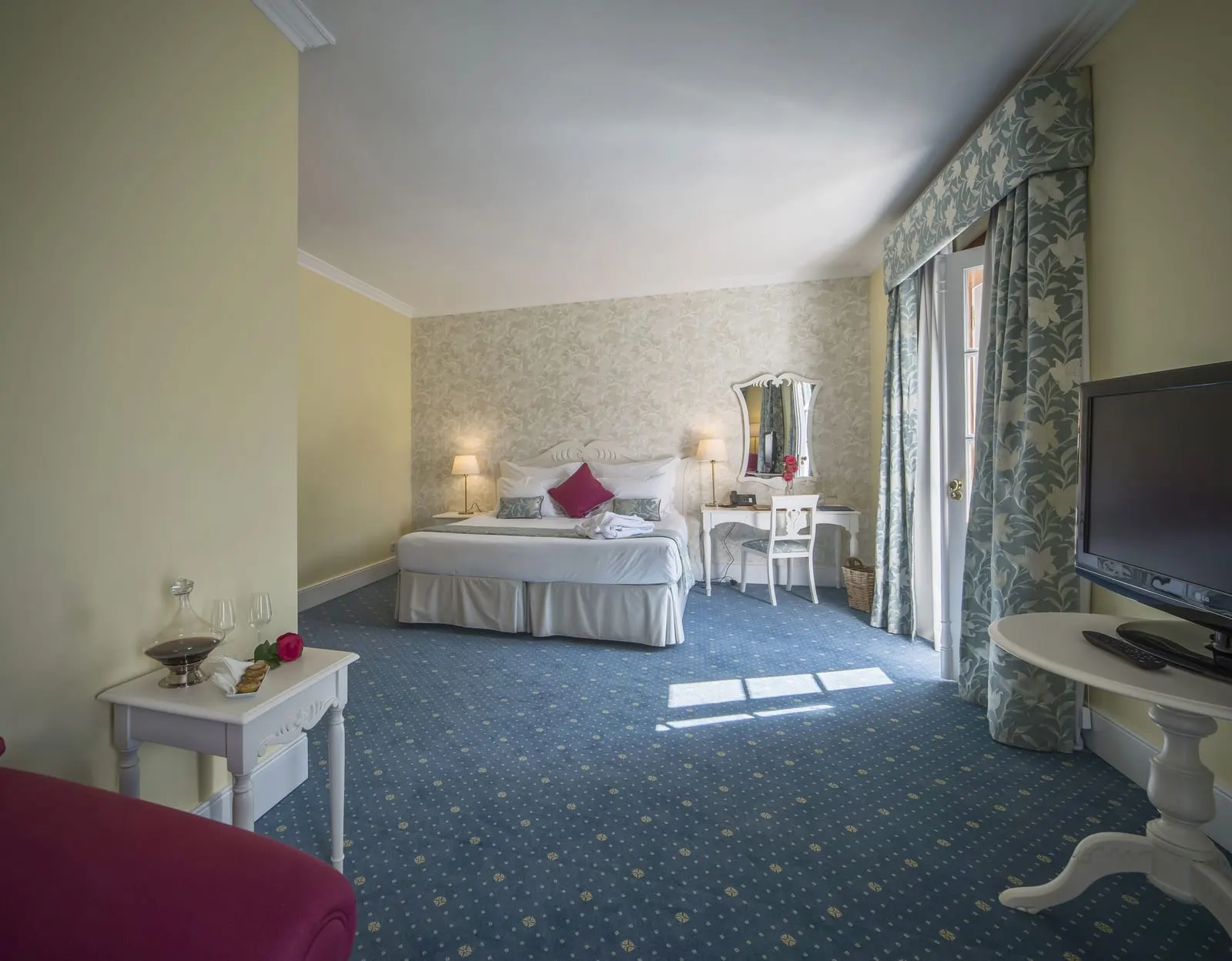 Junior Suite Douro River View at The Vintage House: the bed and dressing table across a blue carpet, with a TV in front
