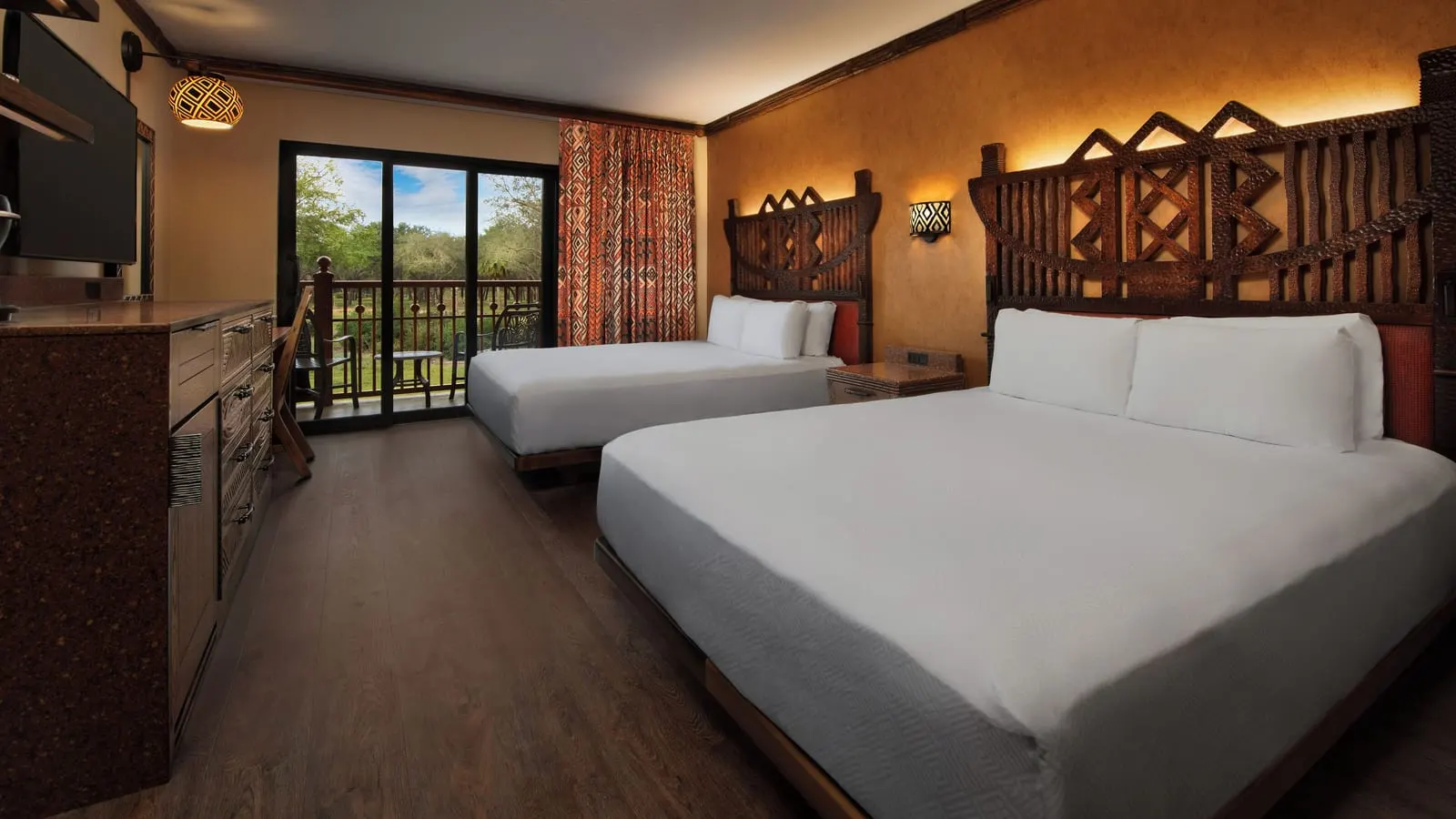 Water View room at Disney's Animal Kingdom Lodge: two queen beds with carved wooden headboards, a chest of drawers, a wall-mounted television and a glass door onto a balcony with two chairs