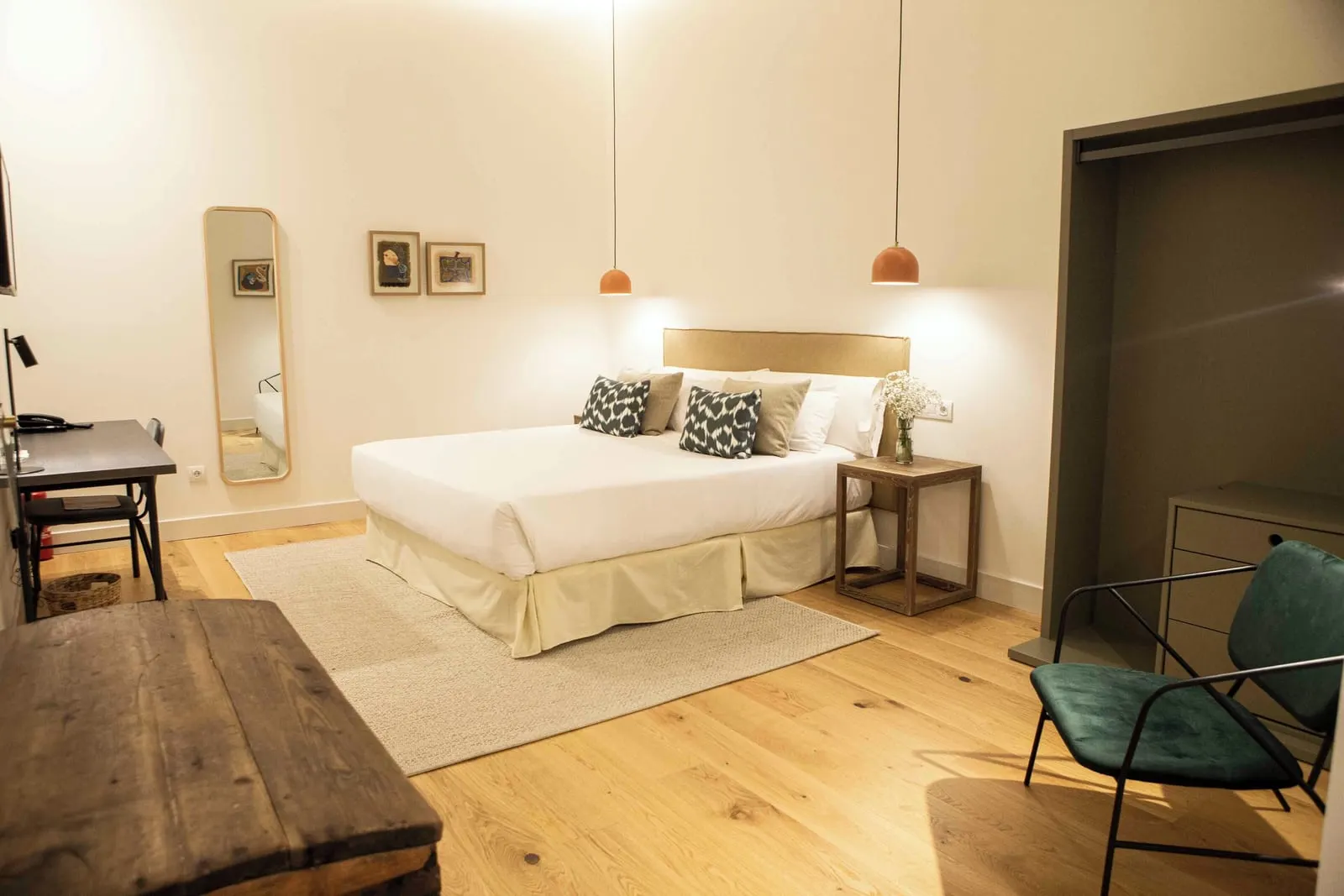 Deluxe Interior at Hotel Veintiuno: a double bed on a rug between terracotta pendant lamps, with a desk and a full-length mirror on one side and an open wardrobe and a green velvet armchair on the other
